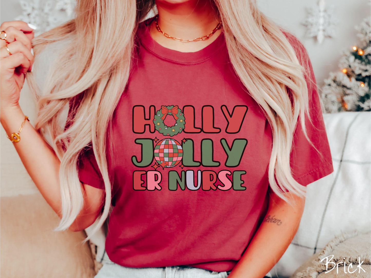 A woman wearing a cute, vintage brick colored Comfort Colors T-shirt with the text Holly Jolly ER Nurse in red, green, pink, and blue font. The letter O in Holly is a Christmas wreath and the letter O in Jolly is a multi-colored disco ball.