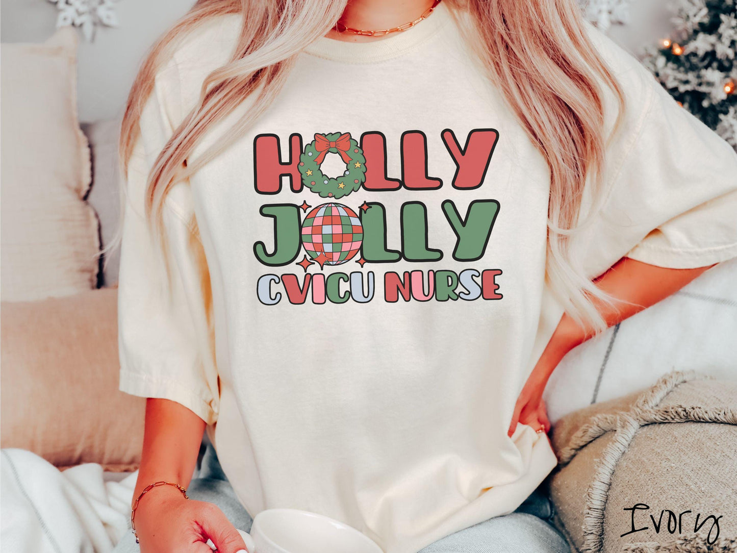 A woman wearing a cute, vintage ivory colored Comfort Colors T-shirt with the text Holly Jolly CVICU Nurse in red, green, pink, and blue font. The letter O in Holly is a Christmas wreath and the letter O in Jolly is a multi-colored disco ball.