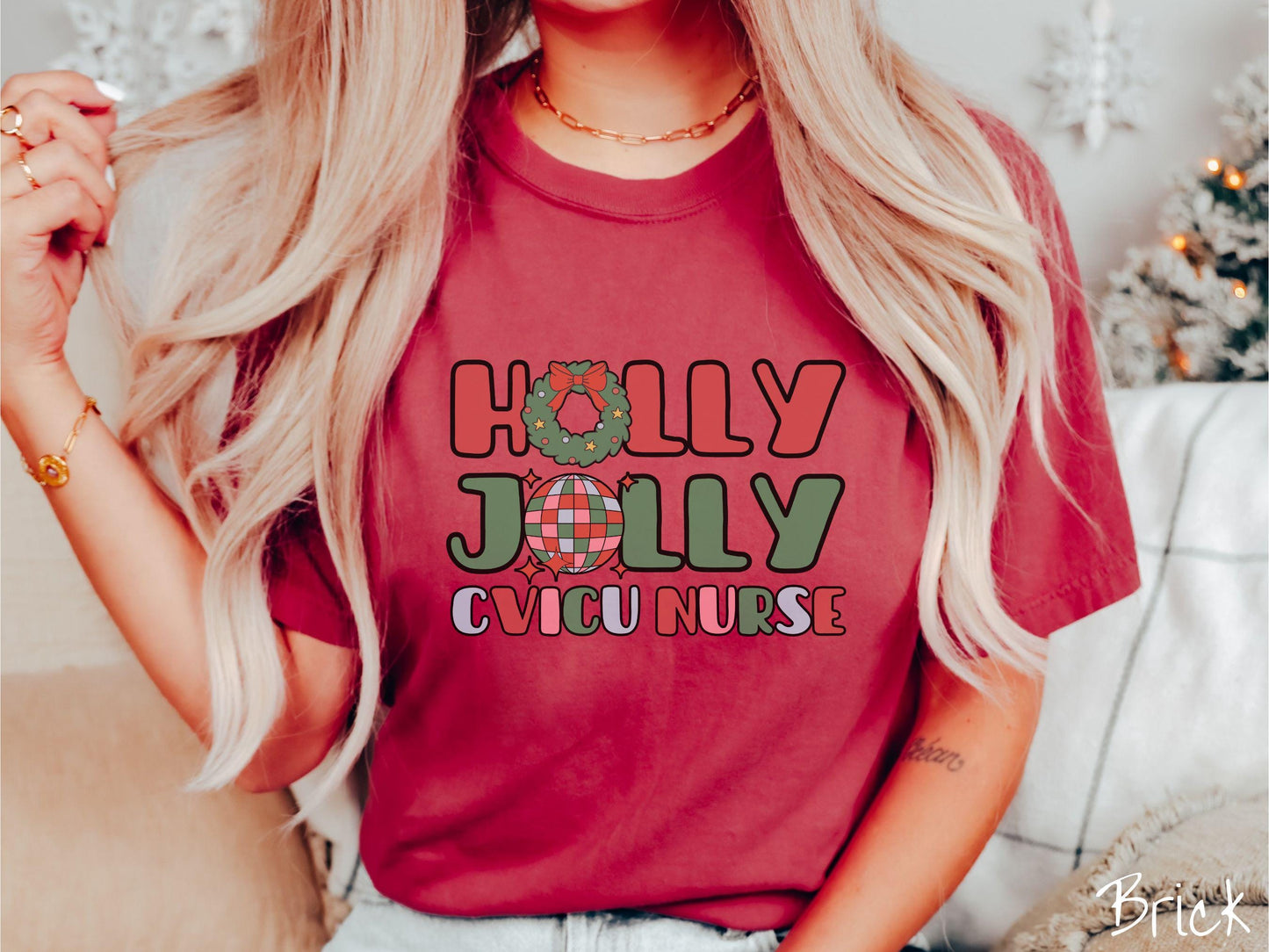 A woman wearing a cute, vintage brick colored Comfort Colors T-shirt with the text Holly Jolly CVICU Nurse in red, green, pink, and blue font. The letter O in Holly is a Christmas wreath and the letter O in Jolly is a multi-colored disco ball.