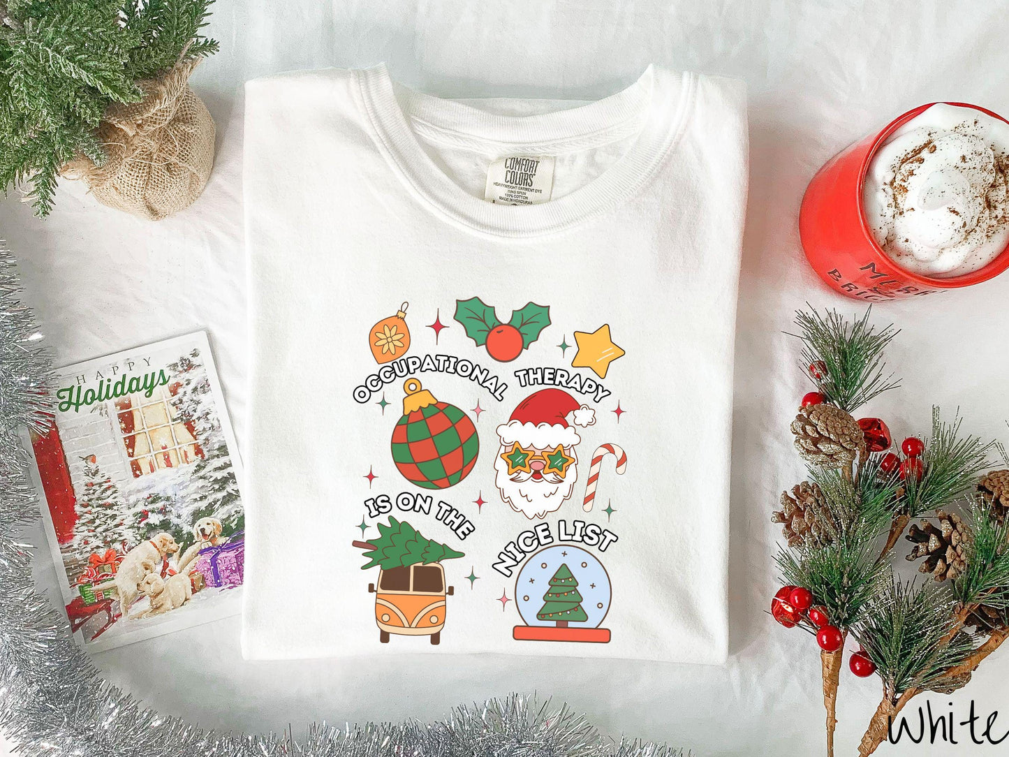 This vintage white colored Comfort Colors T-shirt features the text 'Occupational Therapy is on the nice list' in white font, surrounded by Christmas lights, cranberries, Santa Claus, a candy cane, a snow globe, and other festive decorations.