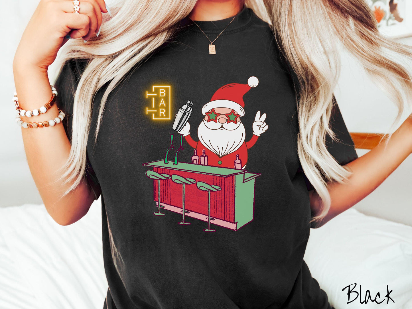 A vintage black colored Comfort Colors T-shirt features Santa Claus with red and green glasses mixing drinks and holding up a peace sign behind a red and green bar.
