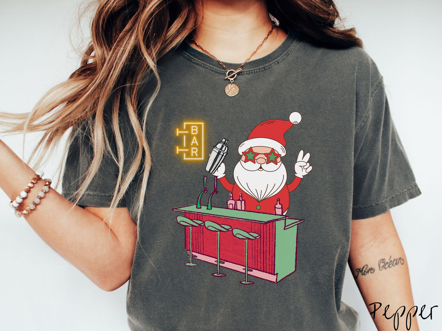 A vintage pepper colored Comfort Colors T-shirt features Santa Claus with red and green glasses mixing drinks and holding up a peace sign behind a red and green bar.