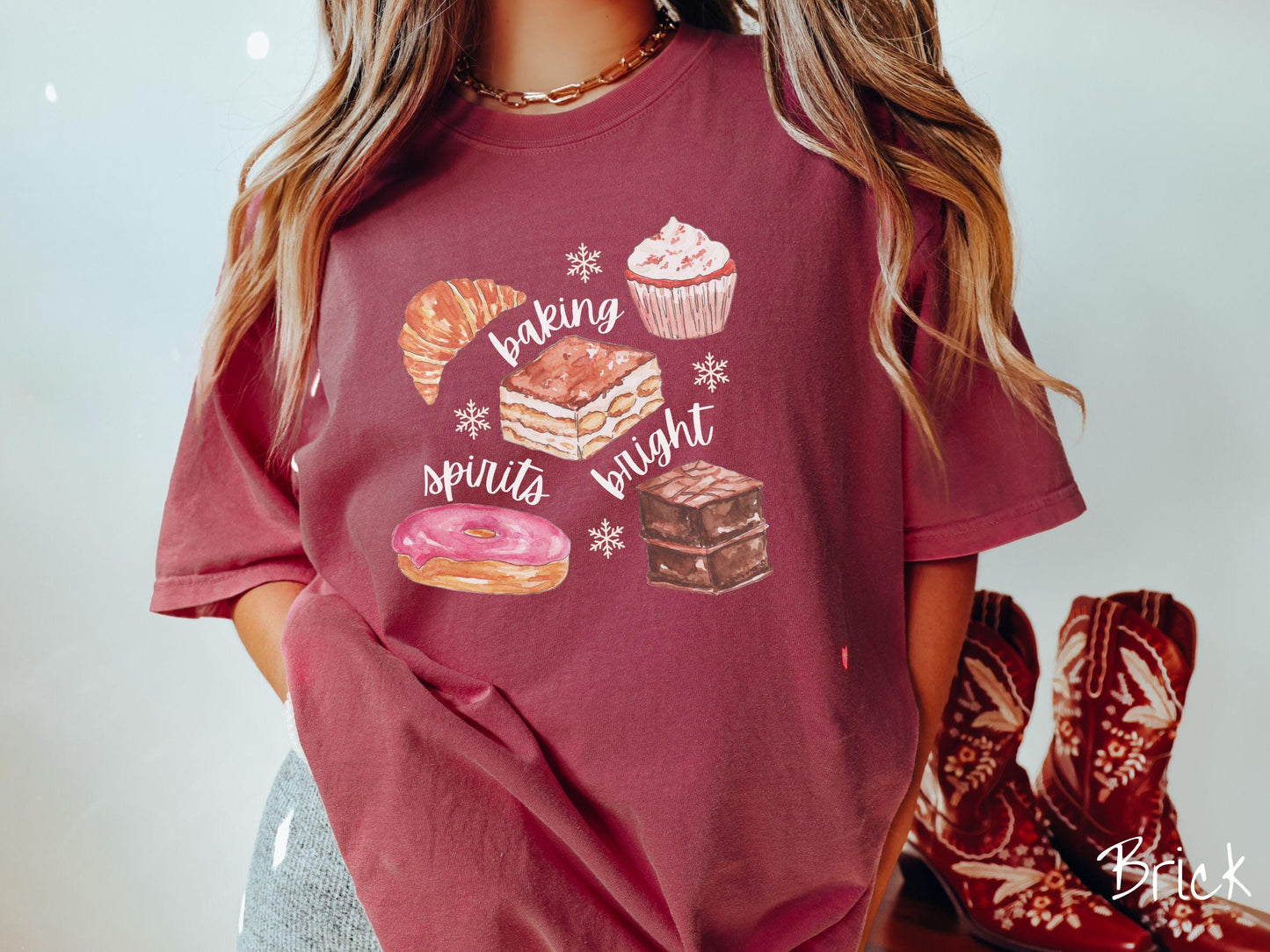 This vintage brick colored Comfort Colors T-shirt features the text 'baking spirits bright' in white cursive font, accompanied by cute dessert illustrations and white snowflakes.