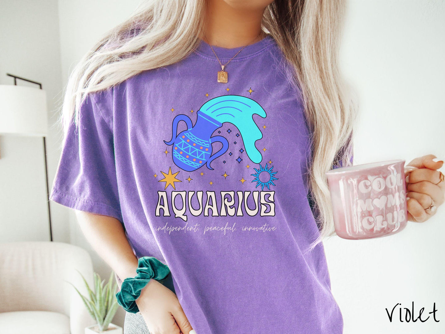 A vintage violet colored Comfort Colors T-shirt features a large purple urn surrounded by stars, with the text Aquarius and the words independent, peaceful, innovative.