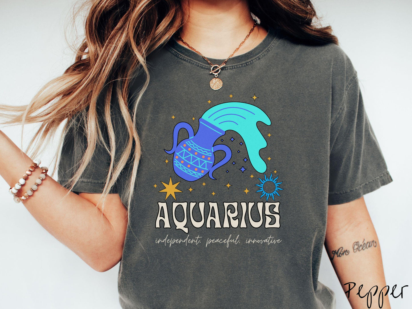 A vintage pepper colored Comfort Colors T-shirt features a large purple urn surrounded by stars, with the text Aquarius and the words independent, peaceful, innovative.