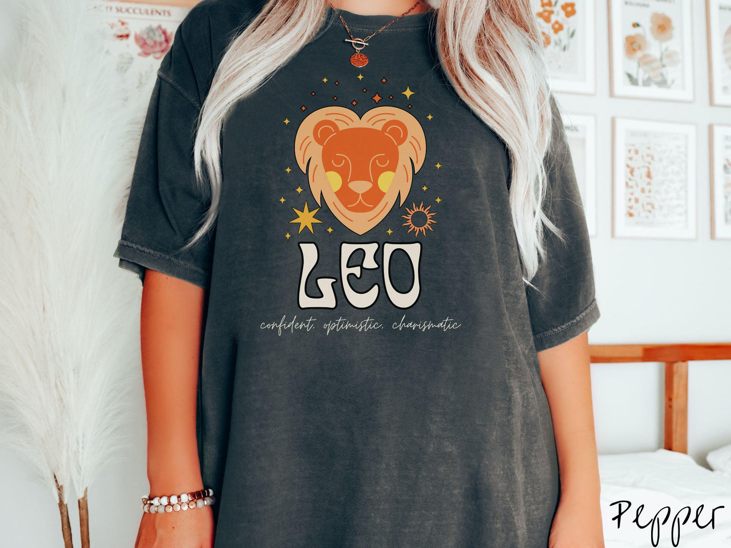 This vintage pepper colored Comfort Colors T-shirt features a large orange and yellow lion surrounded by stars and the sun with the text Leo in large bold font and below that are the words confident, optimistic, charismatic in cursive font.