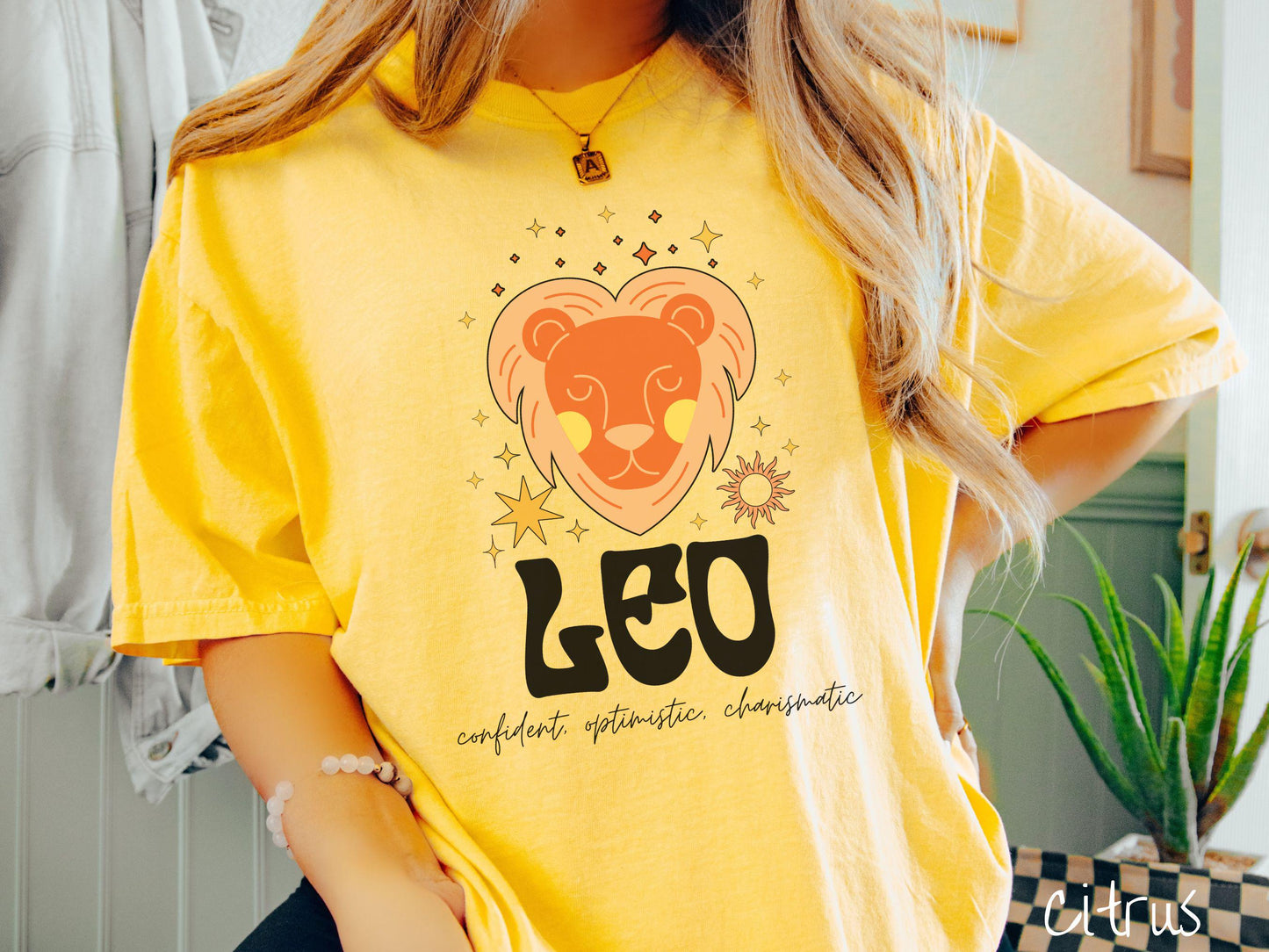 This vintage citrus colored Comfort Colors T-shirt features a large orange and yellow lion surrounded by stars and the sun with the text Leo in large bold font and below that are the words confident, optimistic, charismatic in cursive font.
