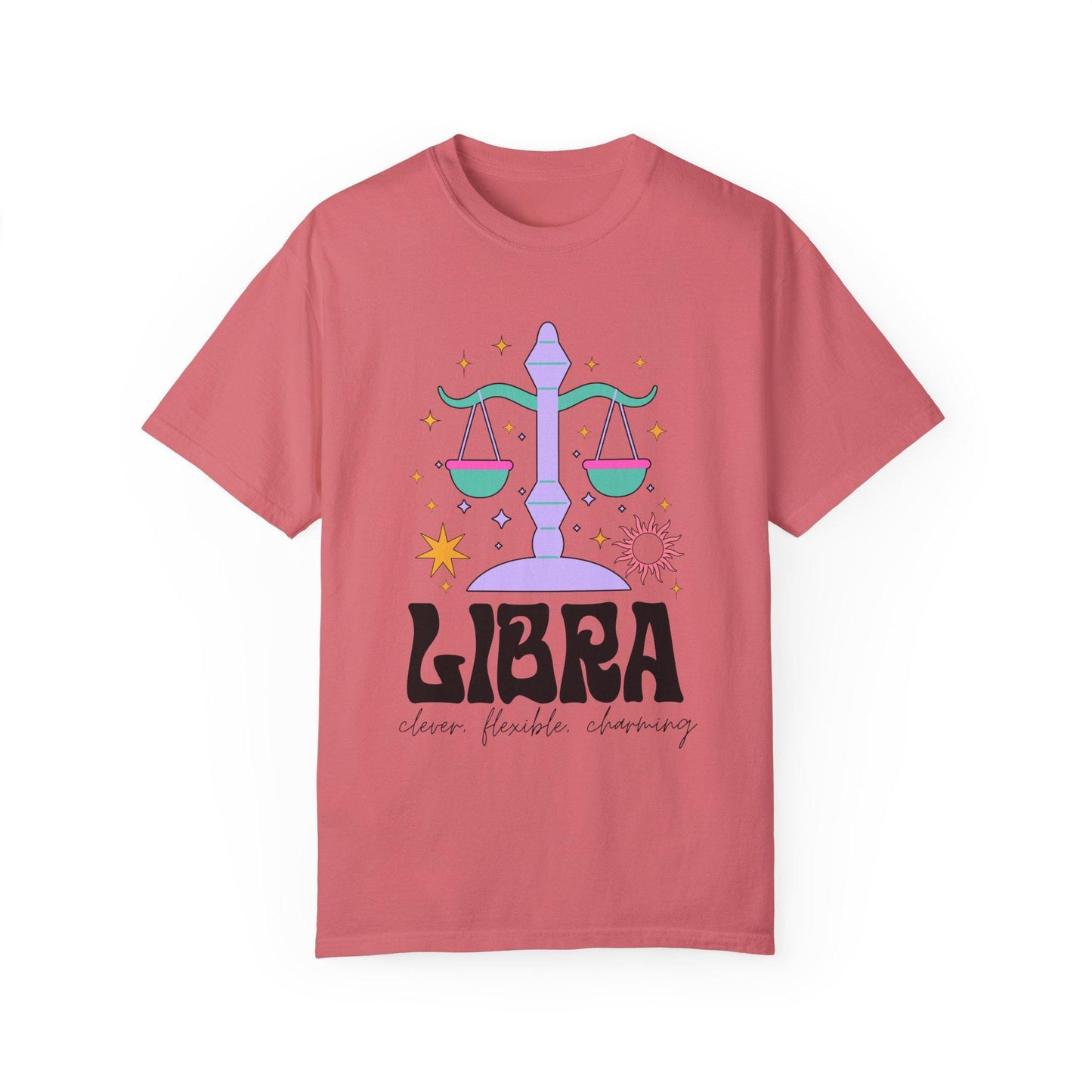 A vintage brick colored Comfort Colors T-shirt features a large purple and green weight scale surrounded by stars and the sun with the text Libra in large bold font and below that are the words clever, flexible, charming in cursive font.