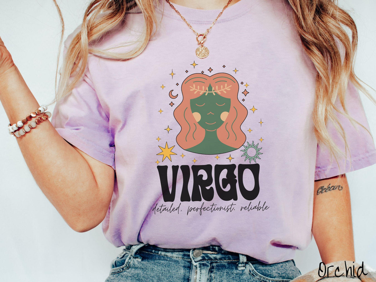 A vintage orchid colored Comfort Colors T-shirt features a green and brown woman wearing a wheat tiara surrounded by stars and the sun with text Virgo in large bold font and below that are the words detailed, perfectionist, reliable in cursive font.