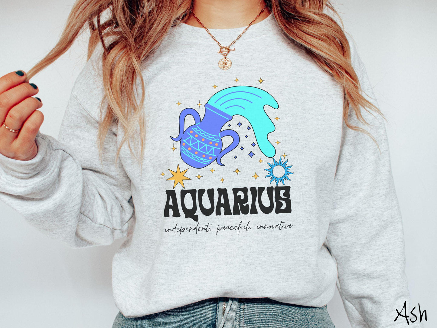 This ash colored vintage Comfort Colors sweatshirt features a large purple urn with blue water flowing out of it, surrounded by stars, with the text Aquarius and the words independent, peaceful, innovative.