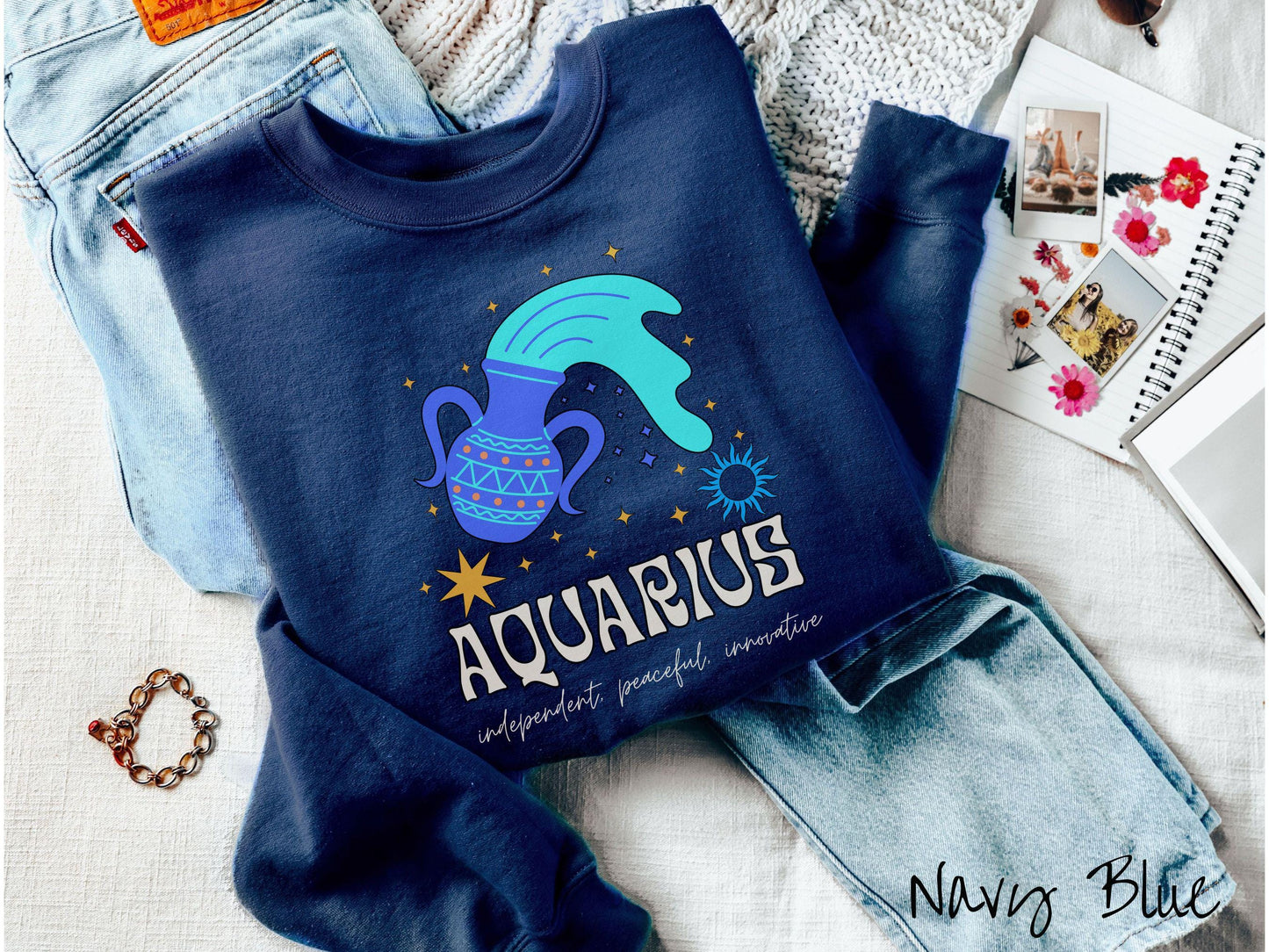 This navy blue colored vintage Comfort Colors sweatshirt features a large purple urn with blue water flowing out of it, surrounded by stars, with the text Aquarius and the words independent, peaceful, innovative.
