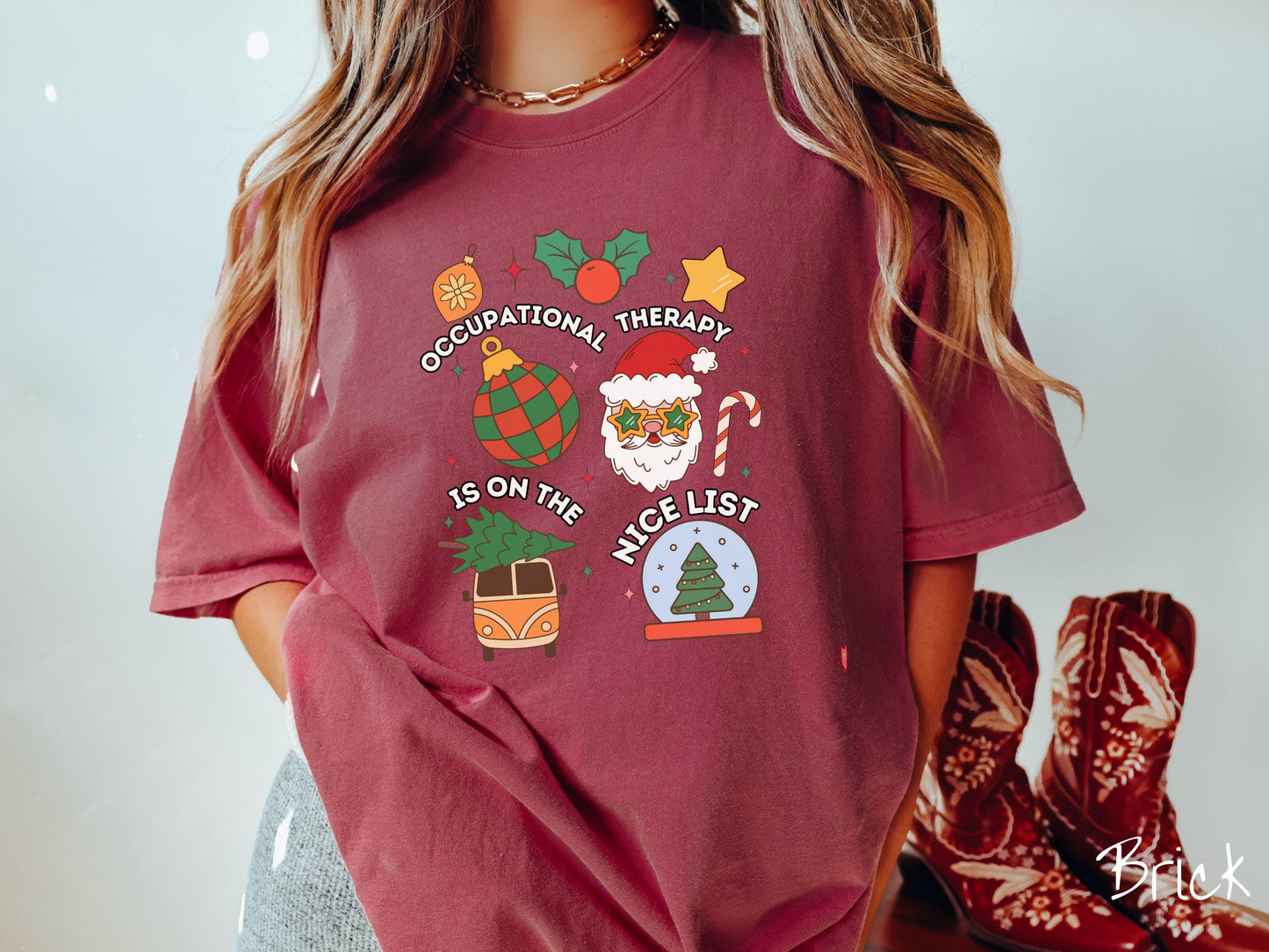 This vintage brick colored Comfort Colors T-shirt features the text 'Occupational Therapy is on the nice list' in white font, surrounded by Christmas lights, cranberries, Santa Claus, a candy cane, a snow globe, and other festive decorations.