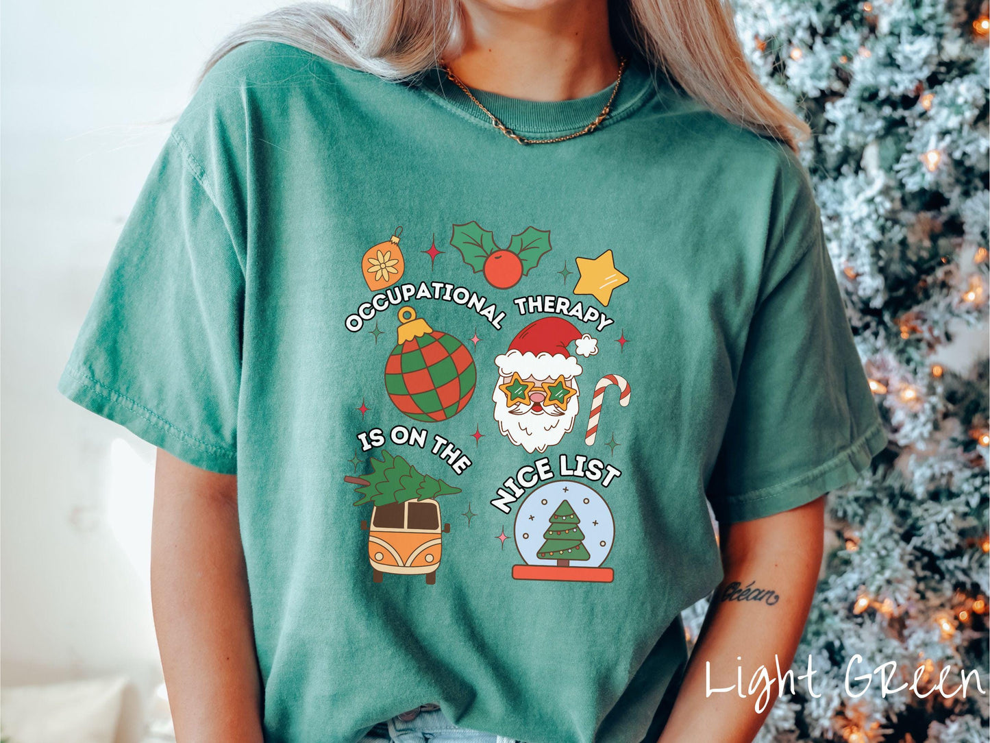 This vintage light green colored Comfort Colors T-shirt features the text 'Occupational Therapy is on the nice list' in white font, surrounded by Christmas lights, cranberries, Santa Claus, a candy cane, a snow globe, and other festive decorations.