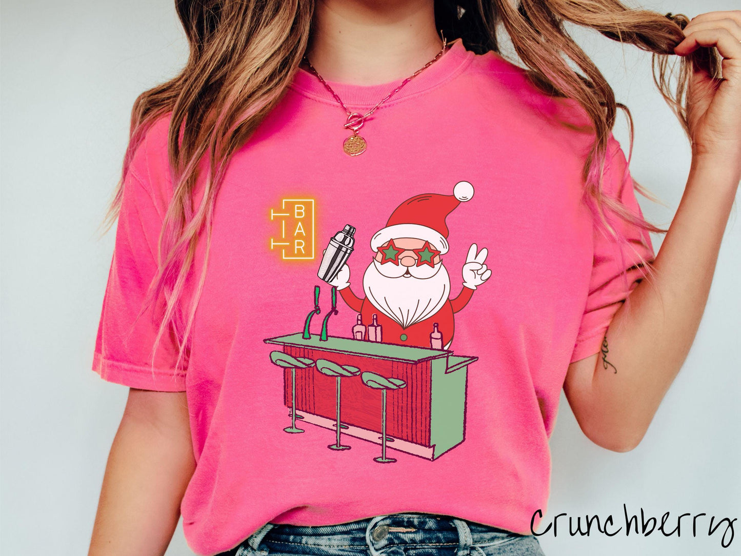 A vintage crunchberry colored Comfort Colors T-shirt features Santa Claus with red and green glasses mixing drinks and holding up a peace sign behind a red and green bar.