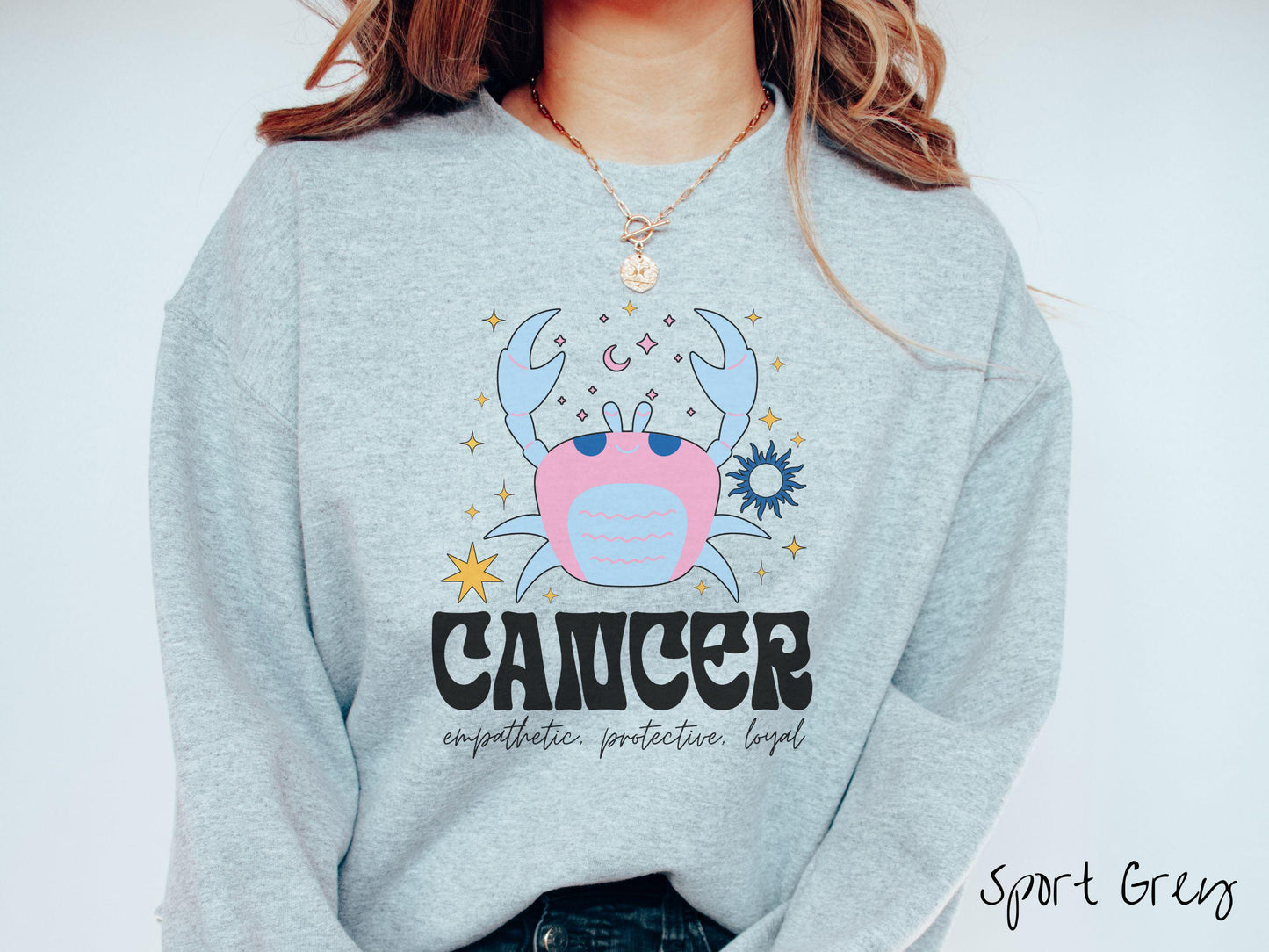 A vintage sport grey colored Comfort Colors sweatshirt features a large pink and blue crab, surrounded by stars, with the text Cancer and the words empathetic, protective, loyal.