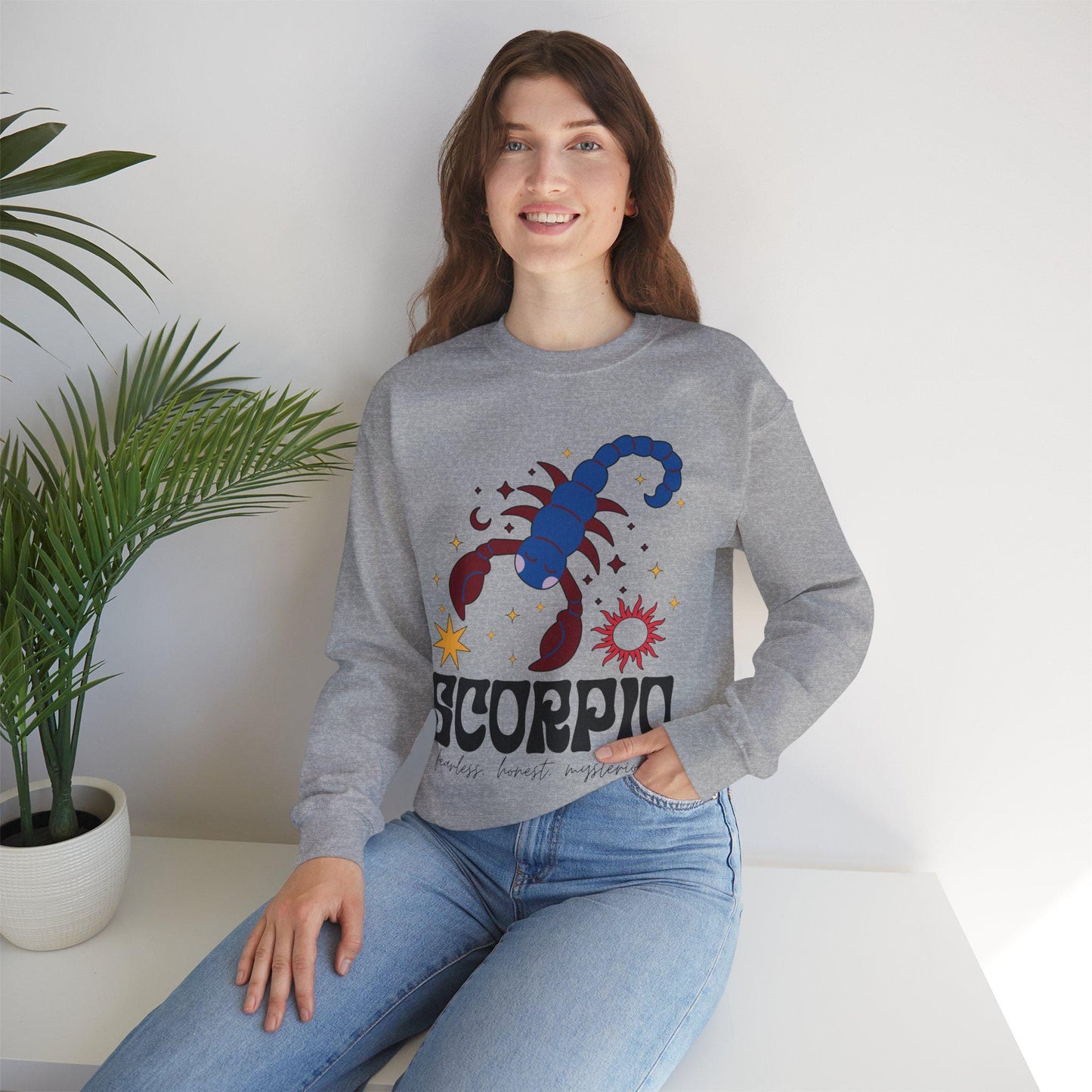 A vintage red colored Gildan sweatshirt features a large red and blue scorpion surrounded by stars and the sun with the text Scorpio in large bold font and below that are the words fearless, honest, mysterious in cursive font.