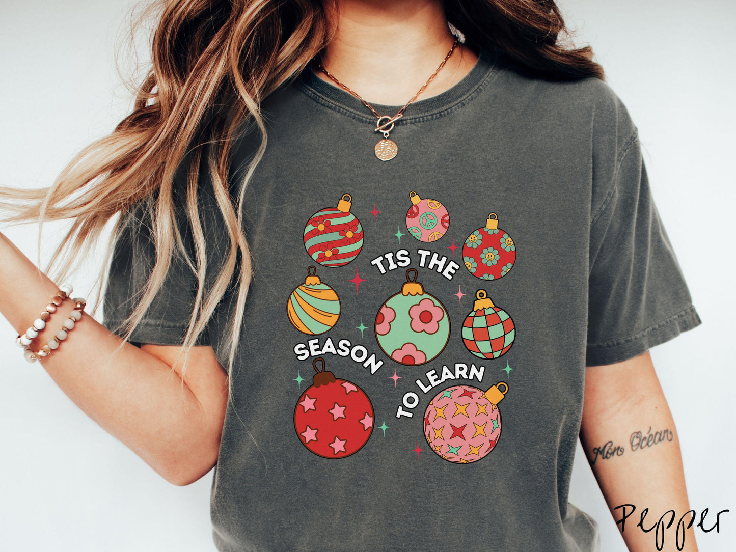 This vintage pepper colored Comfort Colors T-shirt features eight colorful Christmas tree ornaments arranged in a grid pattern and twinkling stars with the text Tis the Season to Learn.
