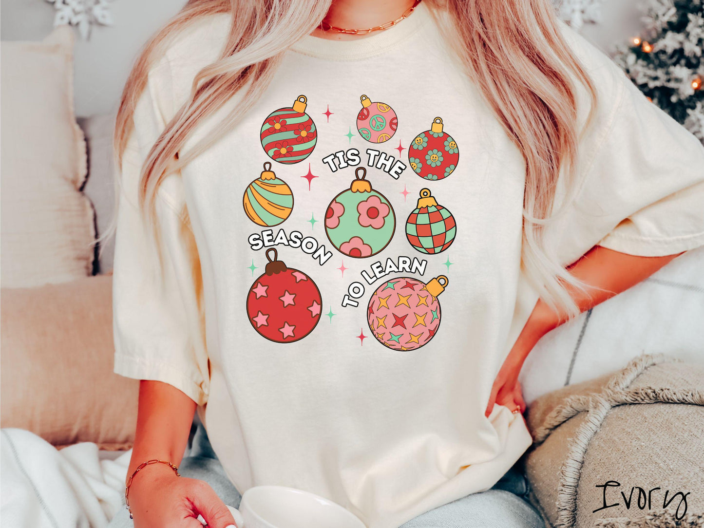 This vintage ivory colored Comfort Colors T-shirt features eight colorful Christmas tree ornaments arranged in a grid pattern and twinkling stars with the text Tis the Season to Learn.