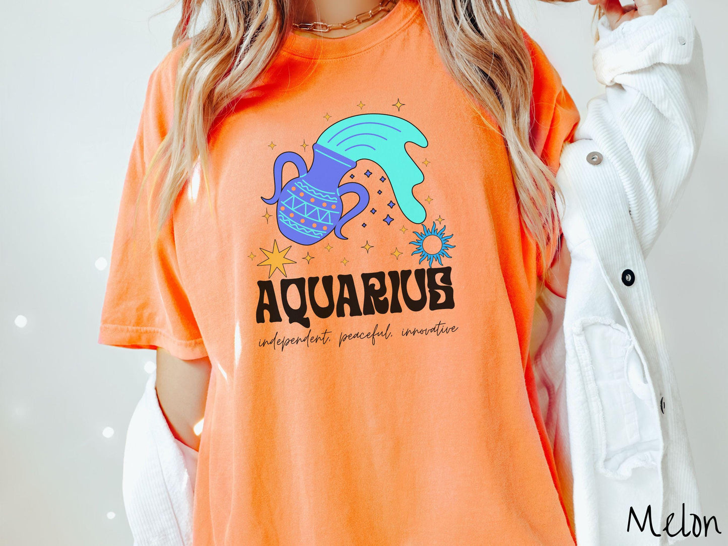 A vintage melon colored Comfort Colors T-shirt features a large purple urn surrounded by stars, with the text Aquarius and the words independent, peaceful, innovative.
