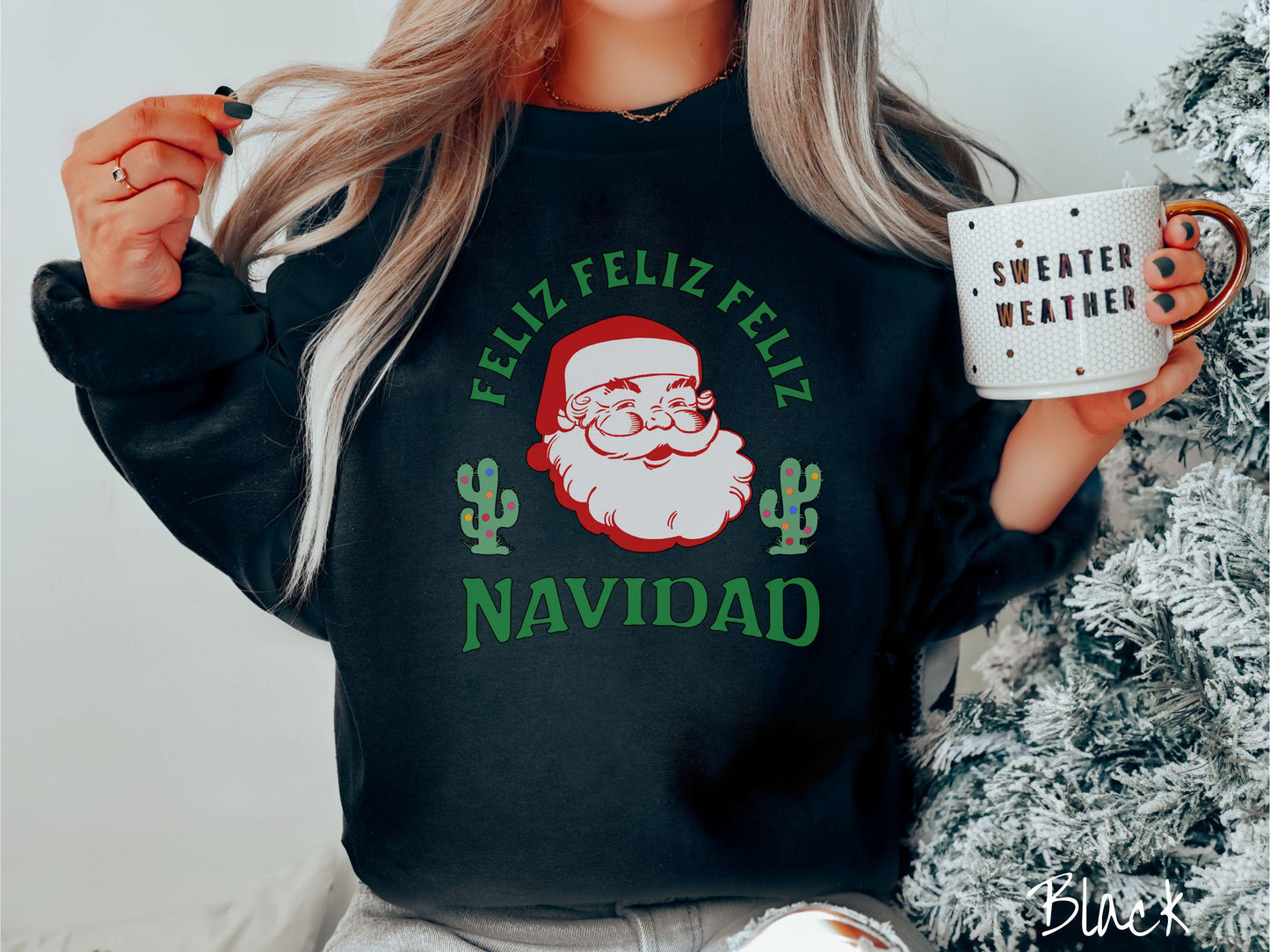 A festive black colored Gildan sweatshirt featuring a smiling santa clause between two green cacti covered in colorful Christmas lights and the phrase, 'Feliz feliz feliz Navidad' is perfect for spreading holiday cheer.