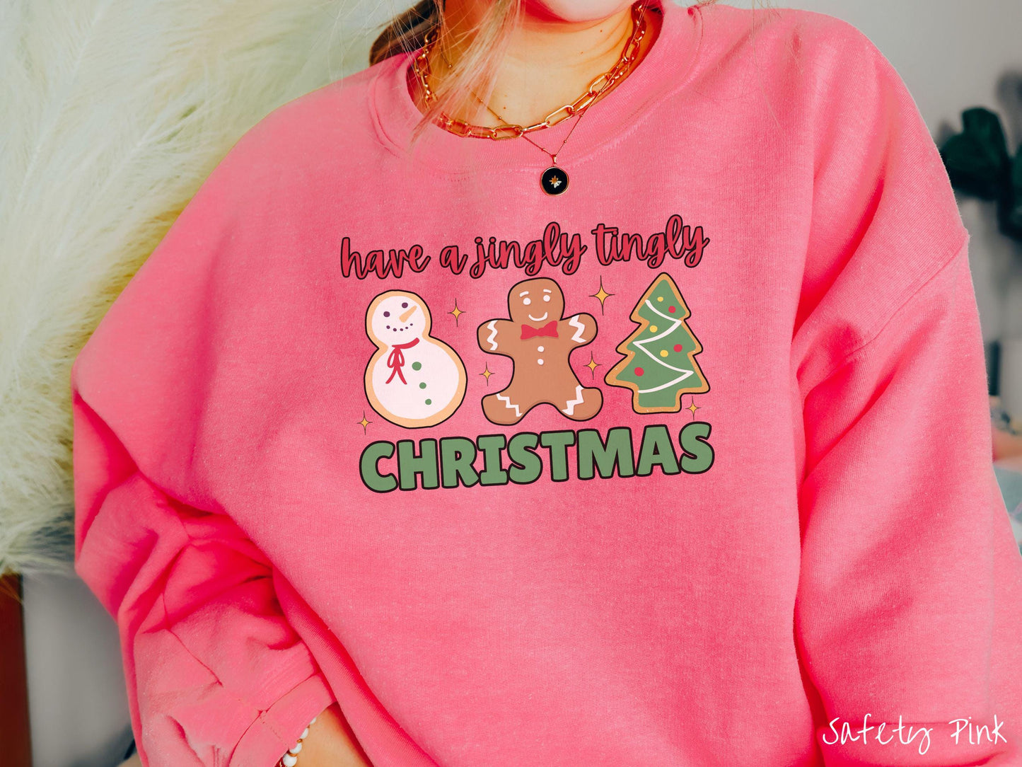A vintage safety pink colored Christmas Gildan sweatshirt featuring a snowman iced cookie, a gingerbread man cookie, and a Christmas tree cookie. The text reads 'have a jingly tingly Christmas' in red and green font.