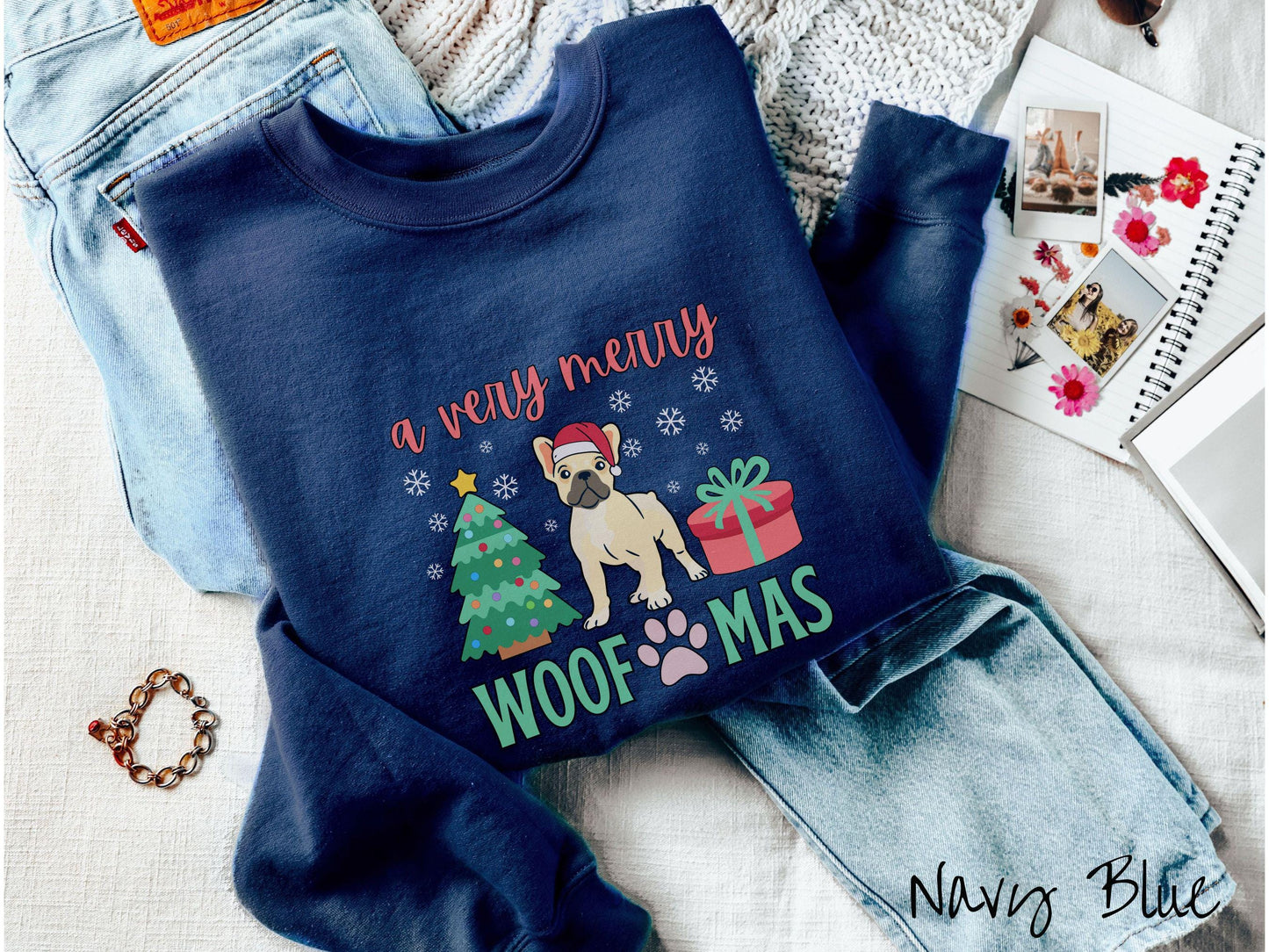 A vintage navy blue colored Gildan sweatshirt with the text 'a very merry Woofmas' in red and green font, featuring a French Bulldog wearing a red Santa hat sitting between a Christmas tree and a present with white snowflakes hanging in the air.