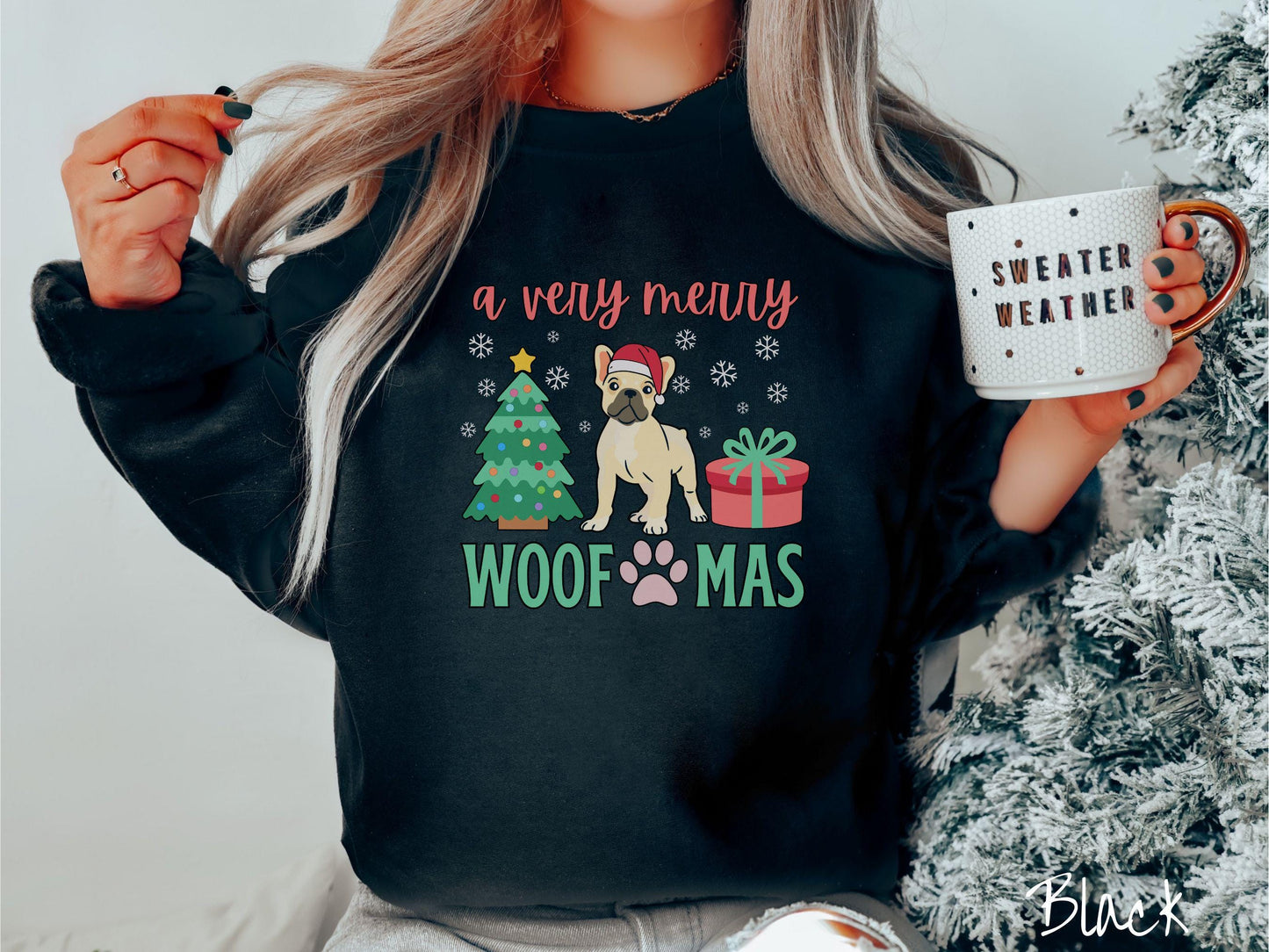 A vintage black colored Gildan sweatshirt with text 'a very merry Woofmas' in red and green font, featuring a French Bulldog wearing a red Santa hat sitting between a decorated Christmas tree and a present with white snowflakes hanging in the air.