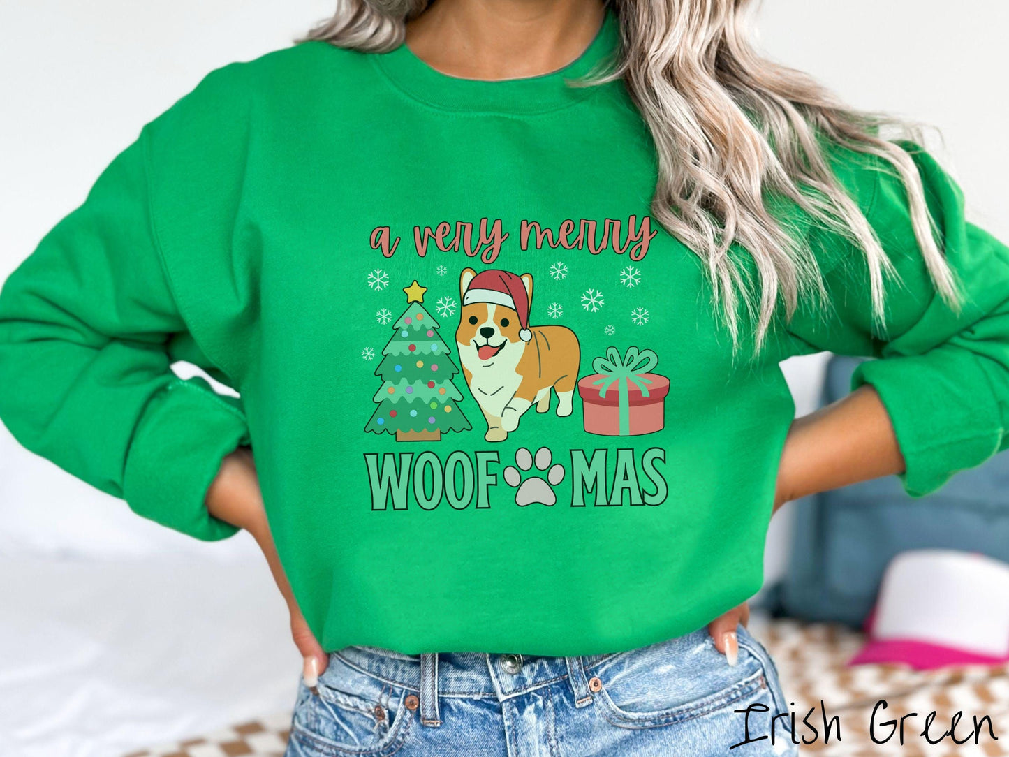 A vintage Irish green colored Gildan sweatshirt with the text 'a very merry Woofmas' in red and green font, featuring an orange corgi wearing a red Santa hat sitting between a Christmas tree and a present with white snowflakes hanging in the air.