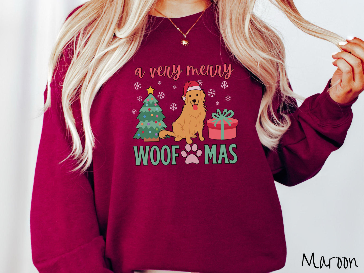 A vintage maroon colored Gildan sweatshirt with the text 'a very merry Woofmas' in red and green font, featuring a Golden Retriever wearing a red Santa hat sitting between a Christmas tree and a present with white snowflakes hanging in the air.