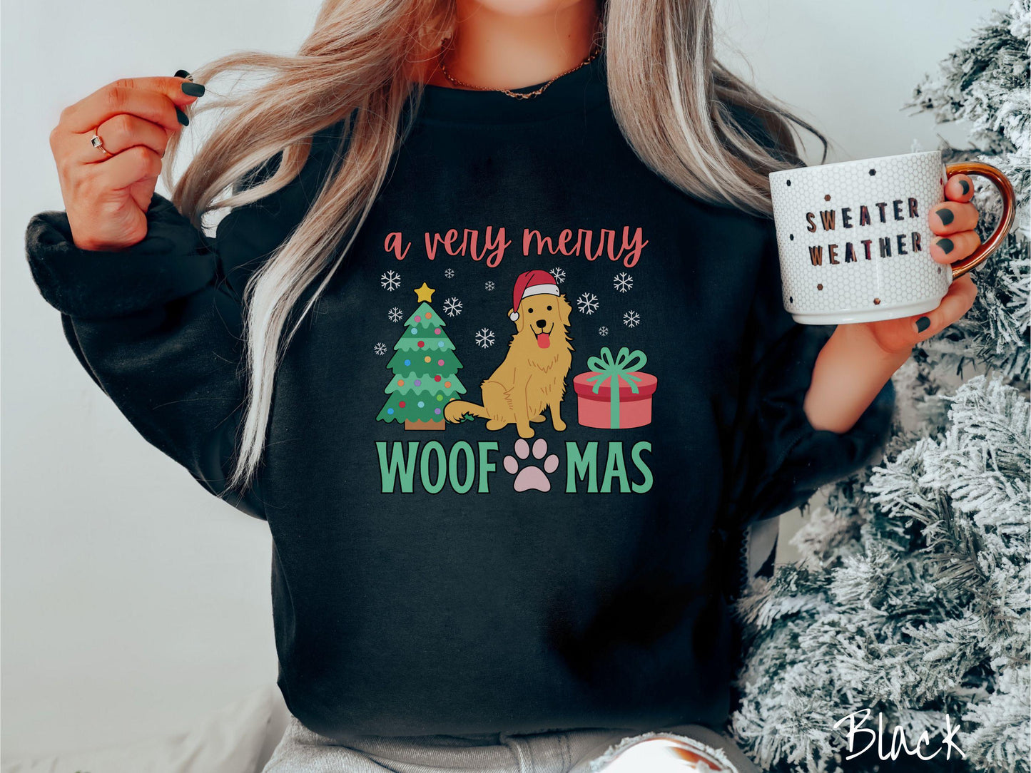 A vintage black colored Gildan sweatshirt with the text 'a very merry Woofmas' in red and green font, featuring a Golden Retriever wearing a red Santa hat sitting between a Christmas tree and a present with white snowflakes hanging in the air.