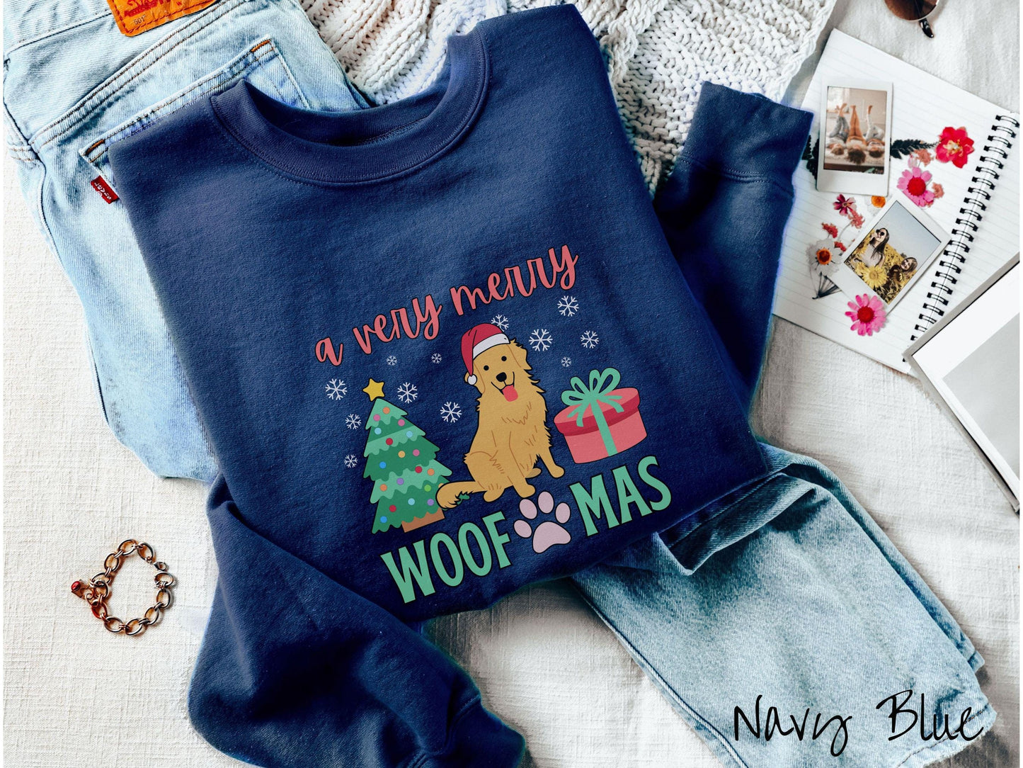 A vintage navy blue colored Gildan sweatshirt with the text 'a very merry Woofmas' in red and green font, featuring a Golden Retriever wearing a red Santa hat sitting between a Christmas tree and a present with white snowflakes hanging in the air.