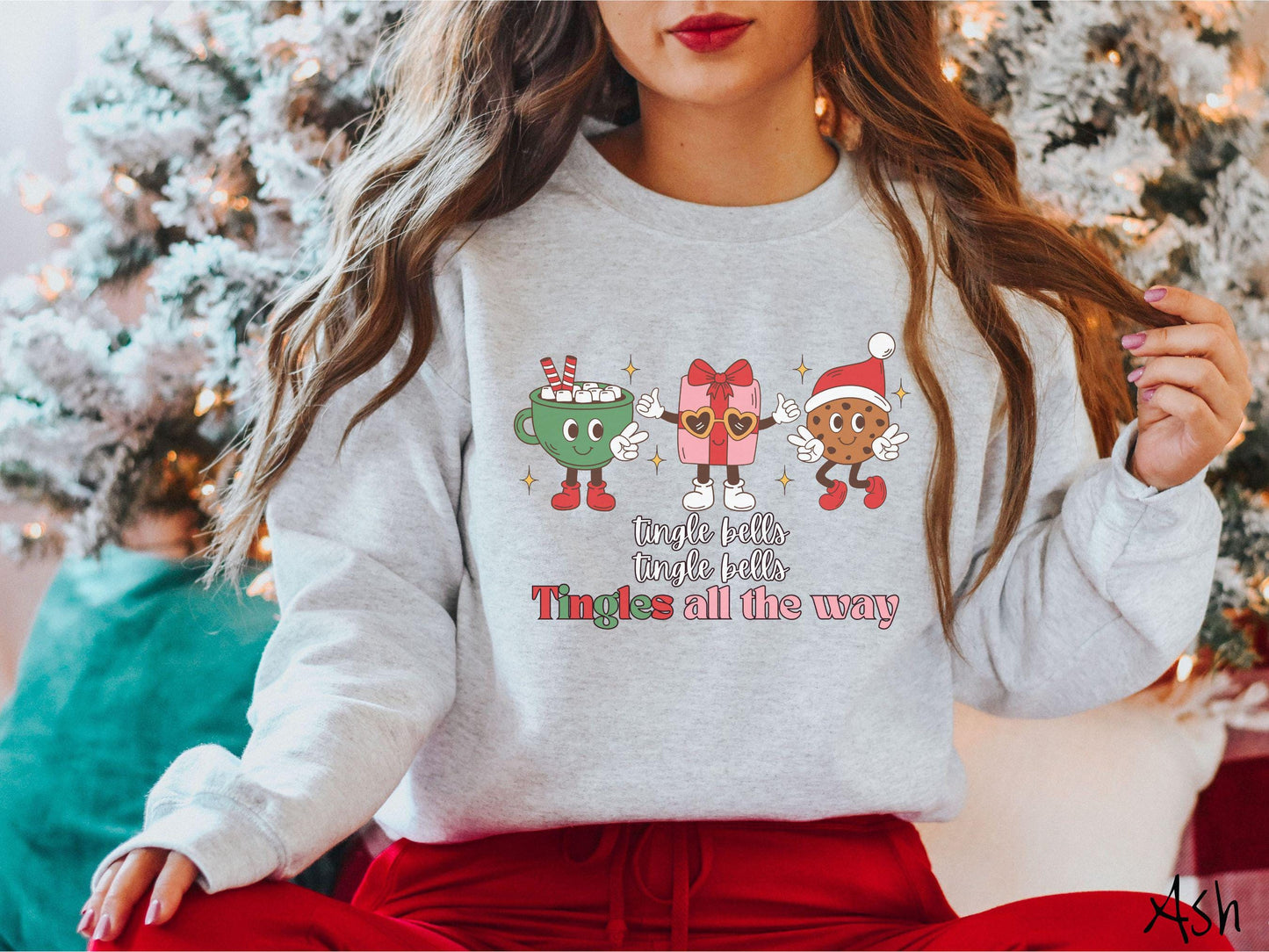 A cute, vintage ash colored Gildan sweatshirt with text tingle bells, tingle bells, Tingles all the way. Above are a green cup of hot cocoa, a red and pink present wearing heart-shaped glasses, and a chocolate chip cookie wearing a Santa hat.