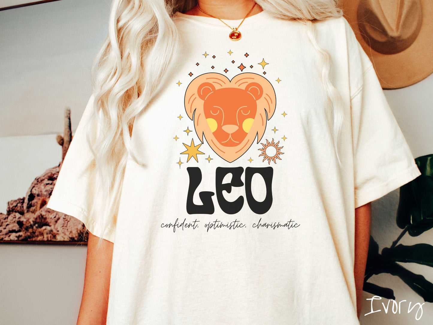 This vintage ivory colored Comfort Colors T-shirt features a large orange and yellow lion surrounded by stars and the sun with the text Leo in large bold font and below that are the words confident, optimistic, charismatic in cursive font.