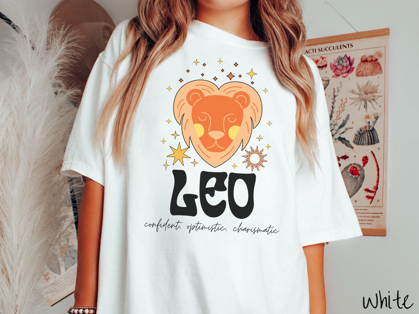 This vintage white colored Comfort Colors T-shirt features a large orange and yellow lion surrounded by stars and the sun with the text Leo in large bold font and below that are the words confident, optimistic, charismatic in cursive font.
