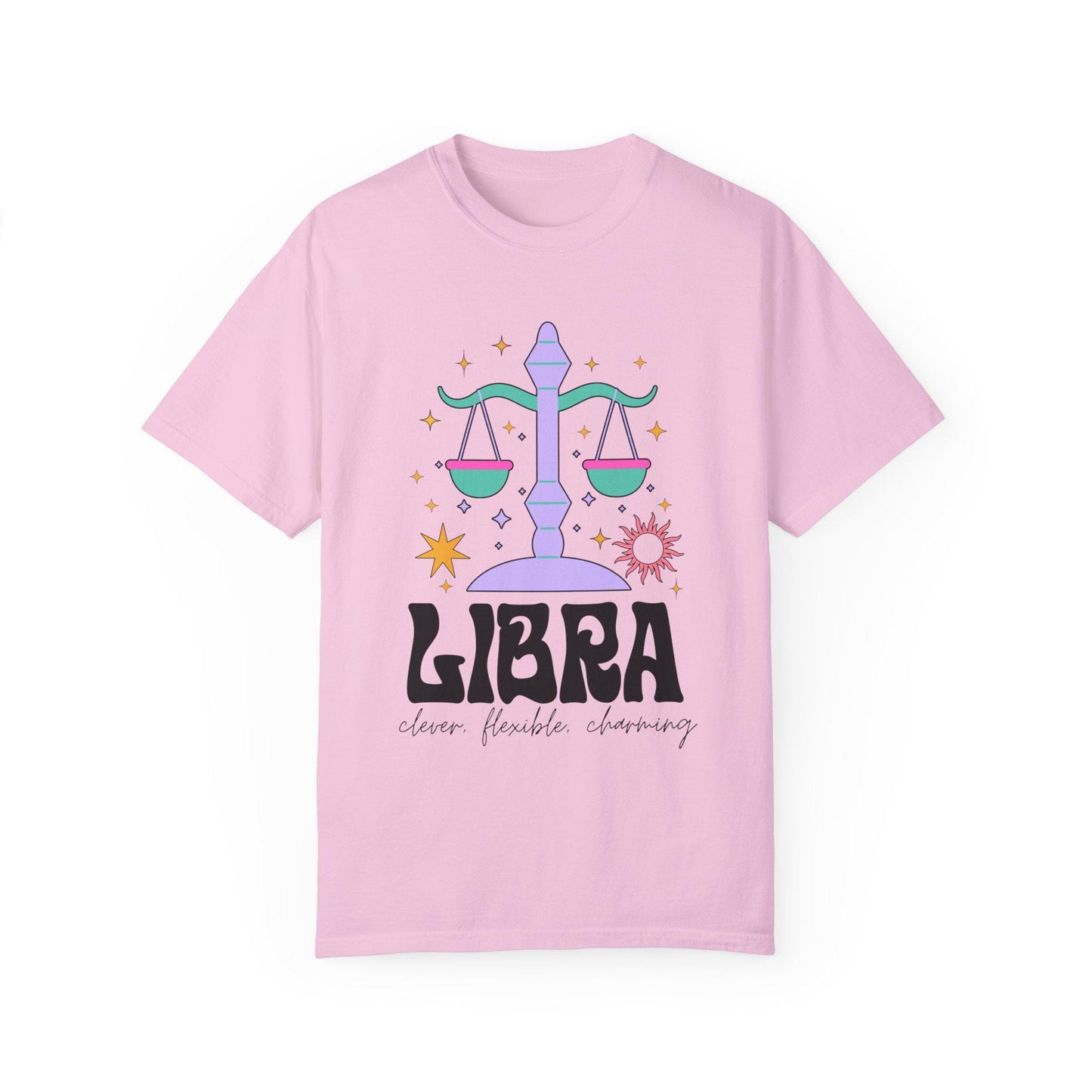 A vintage blossom colored Comfort Colors T-shirt features a large purple and green weight scale surrounded by stars and the sun with the text Libra in large bold font and below that are the words clever, flexible, charming in cursive font.