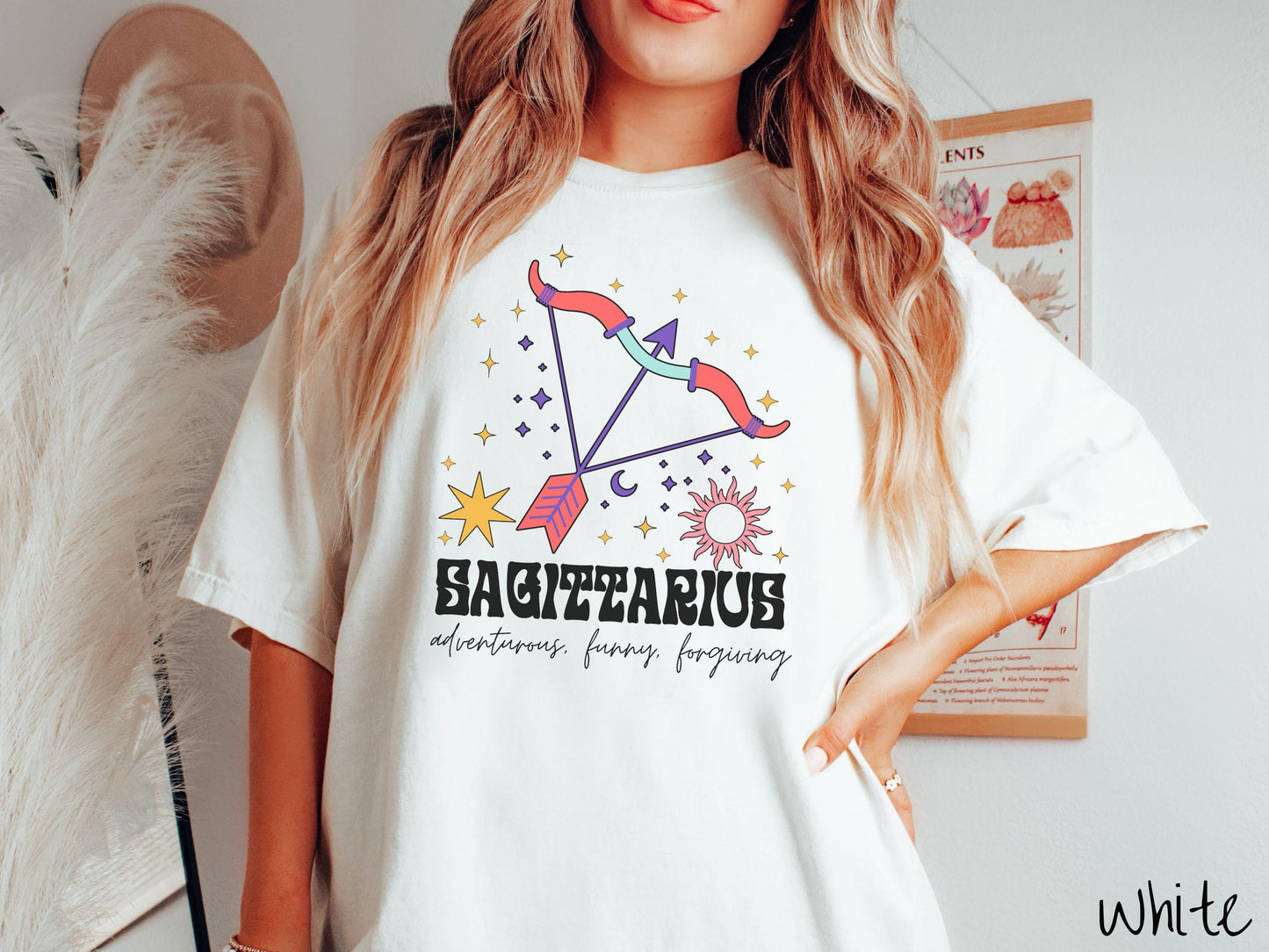 A vintage white colored Comfort Colors T-shirt features a large red and purple bow and arrow surrounded by stars and the sun with the text Sagittarius in large bold font and below that are the words adventurous, funny, forgiving in cursive font.