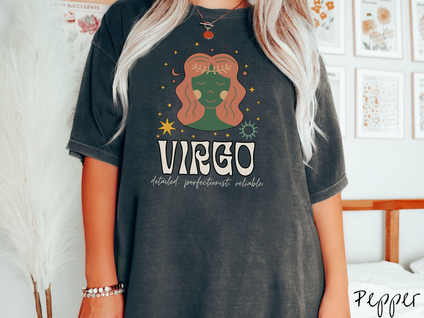 A vintage pepper colored Comfort Colors T-shirt features a green and brown woman wearing a wheat tiara surrounded by stars and the sun with text Virgo in large bold font and below that are the words detailed, perfectionist, reliable in cursive font.