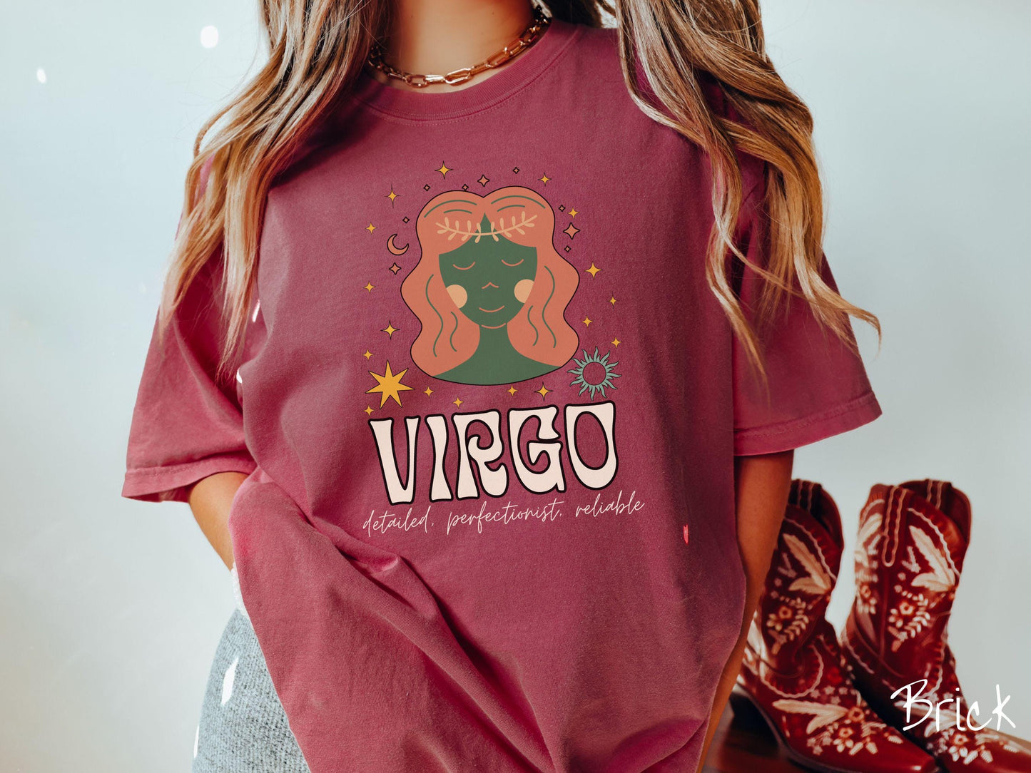 A vintage brick colored Comfort Colors T-shirt features a green and brown woman wearing a wheat tiara surrounded by stars and the sun with text Virgo in large bold font and below that are the words detailed, perfectionist, reliable in cursive font.