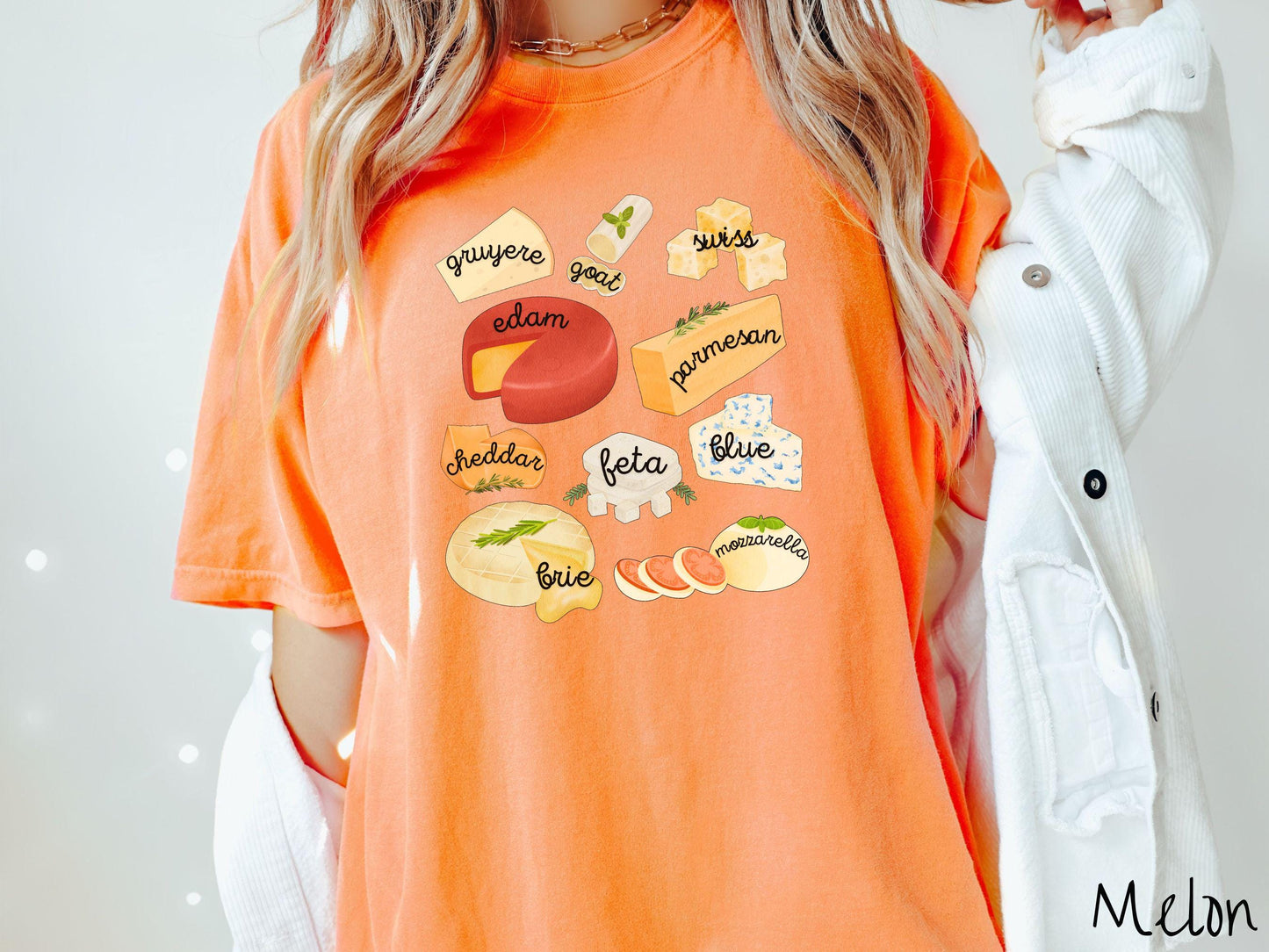 A vintage melon colored T-shirt is perfect for cheese lovers with a grid pattern of various cheeses like feta, parmesan, gruyere, goat, swiss, edam, cheddar, blue, brie, and mozzarella listed.