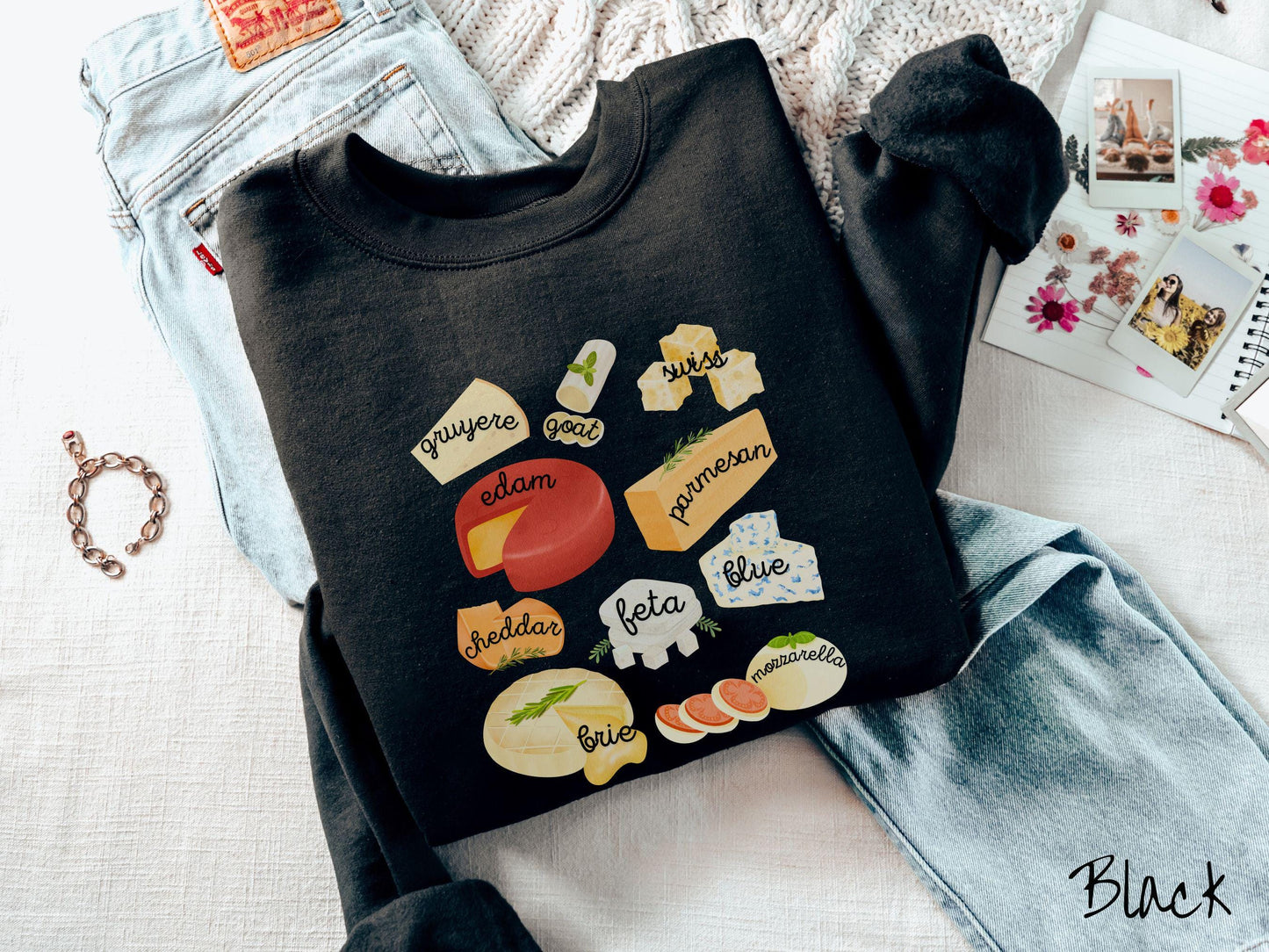 A vintage black colored Gildan sweatshirt is perfect for cheese lovers with a grid pattern of various cheeses like feta, parmesan, gruyere, goat, swiss, edam, cheddar, blue, brie, and mozzarella listed.