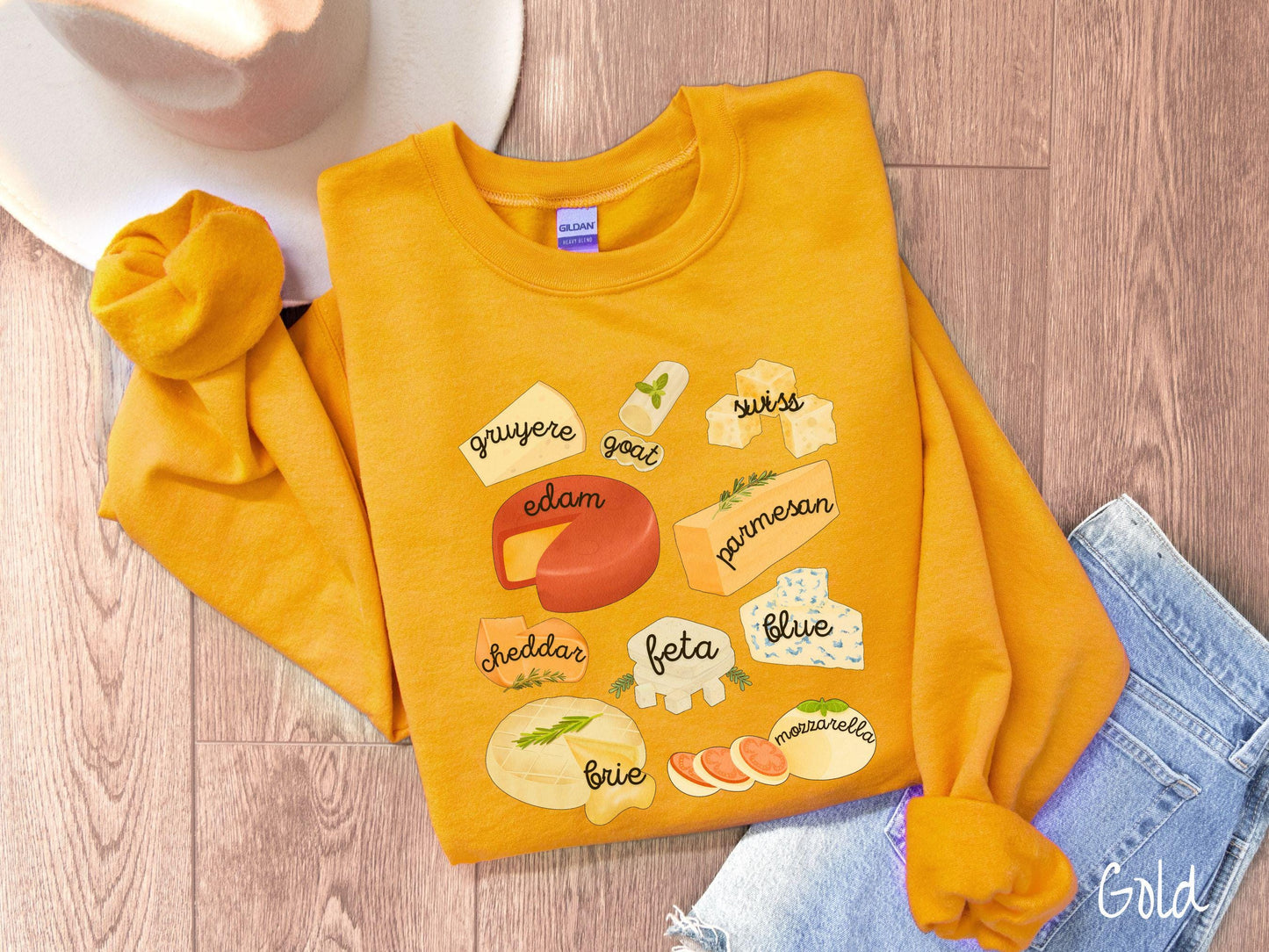 A vintage gold colored Gildan sweatshirt is perfect for cheese lovers with a grid pattern of various cheeses like feta, parmesan, gruyere, goat, swiss, edam, cheddar, blue, brie, and mozzarella listed.