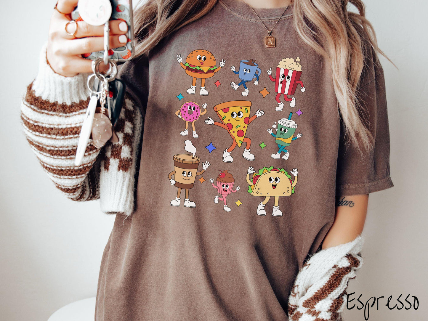 A vintage espresso colored Comfort Colors t-shirt featuring a grid style design of assorted junk foods like a cheeseburger, popcorn, donut, pizza, and a taco, all with smiling faces inside with white gloved hands holding up hand gestures.