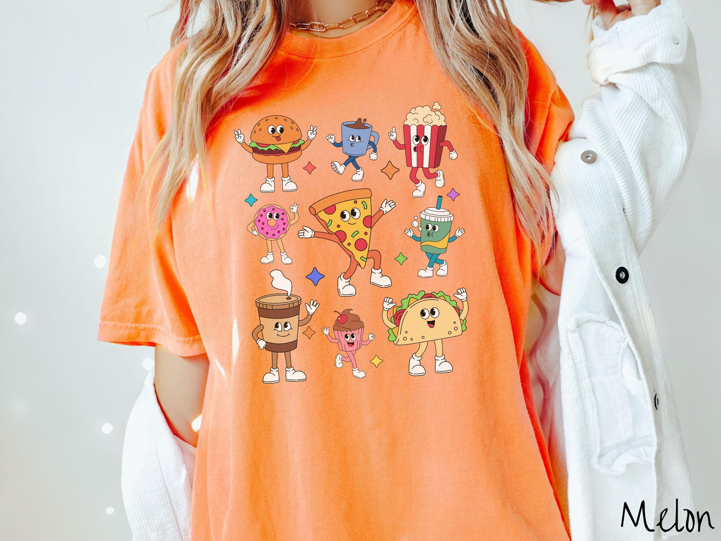 A vintage melon colored Comfort Colors t-shirt featuring a grid style design of assorted junk foods like a cheeseburger, popcorn, donut, pizza, and a taco, all with smiling faces inside with white gloved hands holding up hand gestures.