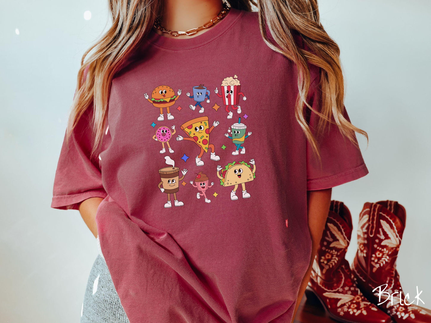 A vintage brick colored Comfort Colors t-shirt featuring a grid style design of assorted junk foods like a cheeseburger, popcorn, donut, pizza, and a taco, all with smiling faces inside with white gloved hands holding up hand gestures.