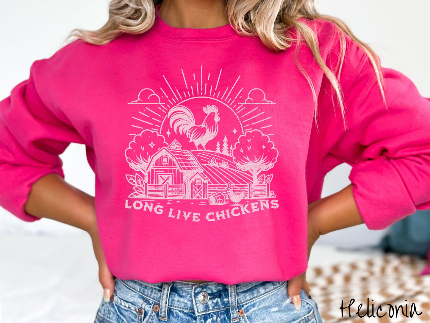 A vintage heliconia colored Gildan sweatshirt featuring a design of a farm with a fence, trees, and plants scattered along the property, a huge chicken in the background at the top of a pasture in front of the sun, and text Long Live Chickens.