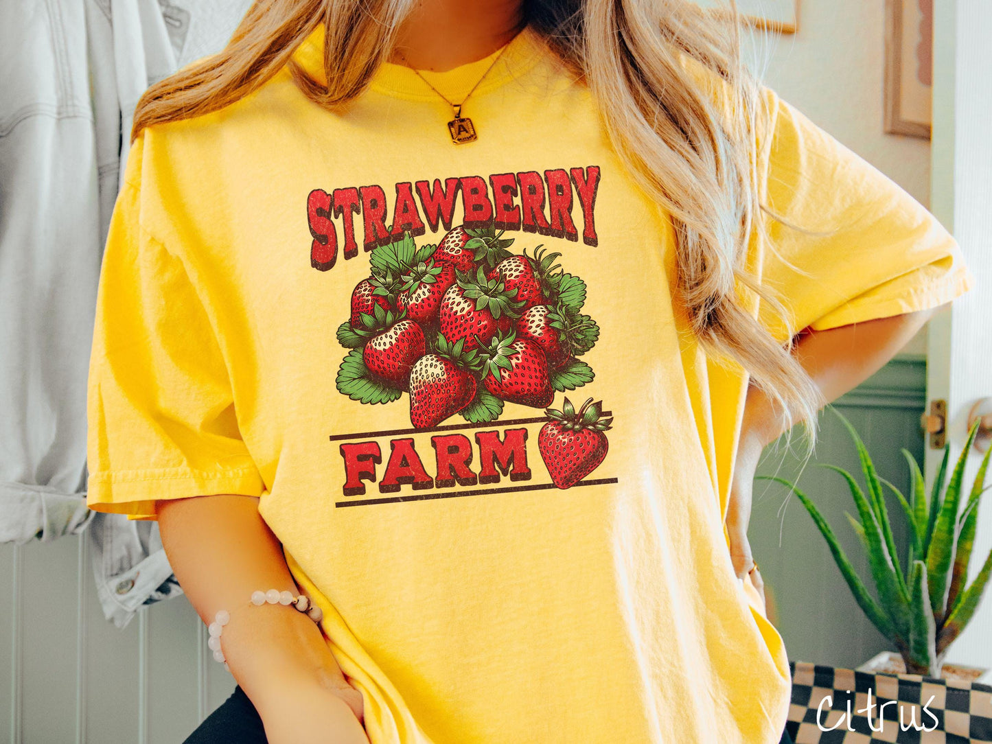 A vintage citrus colored Comfort Colors t-shirt featuring the text Strawberry Farm in red font with a bundle of red strawberries in between the text.