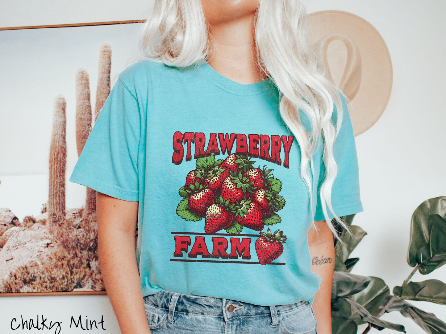 A vintage chalky mint colored Comfort Colors t-shirt featuring the text Strawberry Farm in red font with a bundle of red strawberries in between the text.