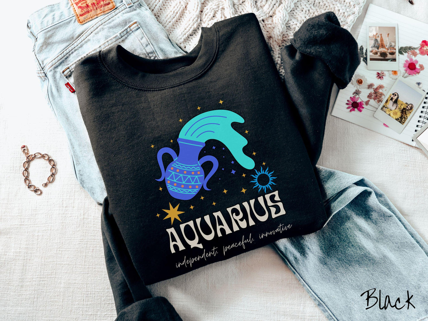 This black colored vintage Comfort Colors sweatshirt features a large purple urn with blue water flowing out of it, surrounded by stars, with the text Aquarius and the words independent, peaceful, innovative.