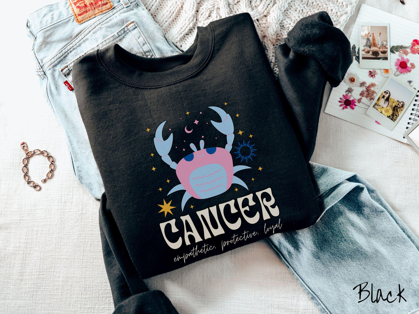 A vintage black colored Comfort Colors sweatshirt features a large pink and blue crab, surrounded by stars, with the text Cancer and the words empathetic, protective, loyal.