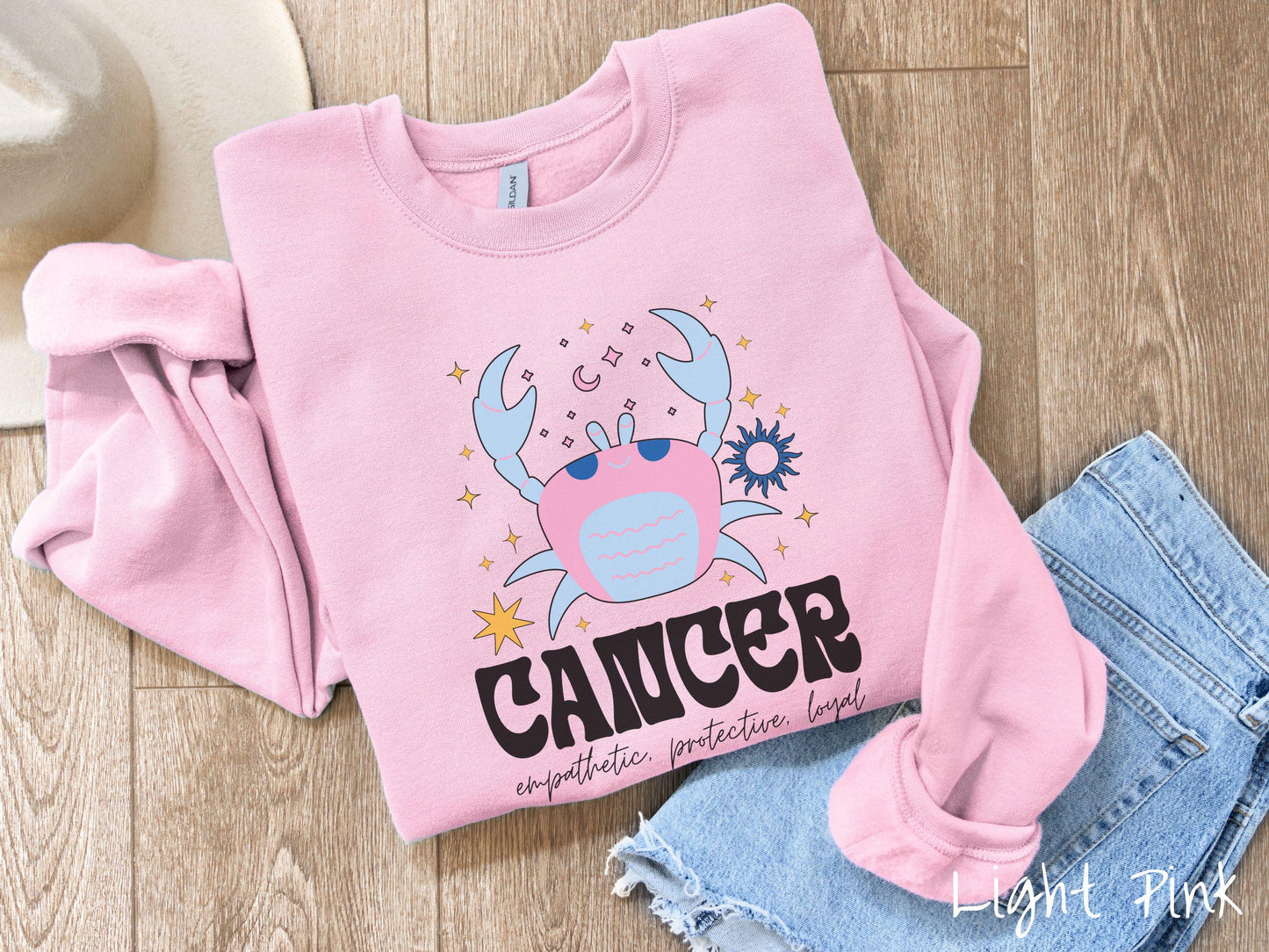 A vintage light pink colored Comfort Colors sweatshirt features a large pink and blue crab, surrounded by stars, with the text Cancer and the words empathetic, protective, loyal.